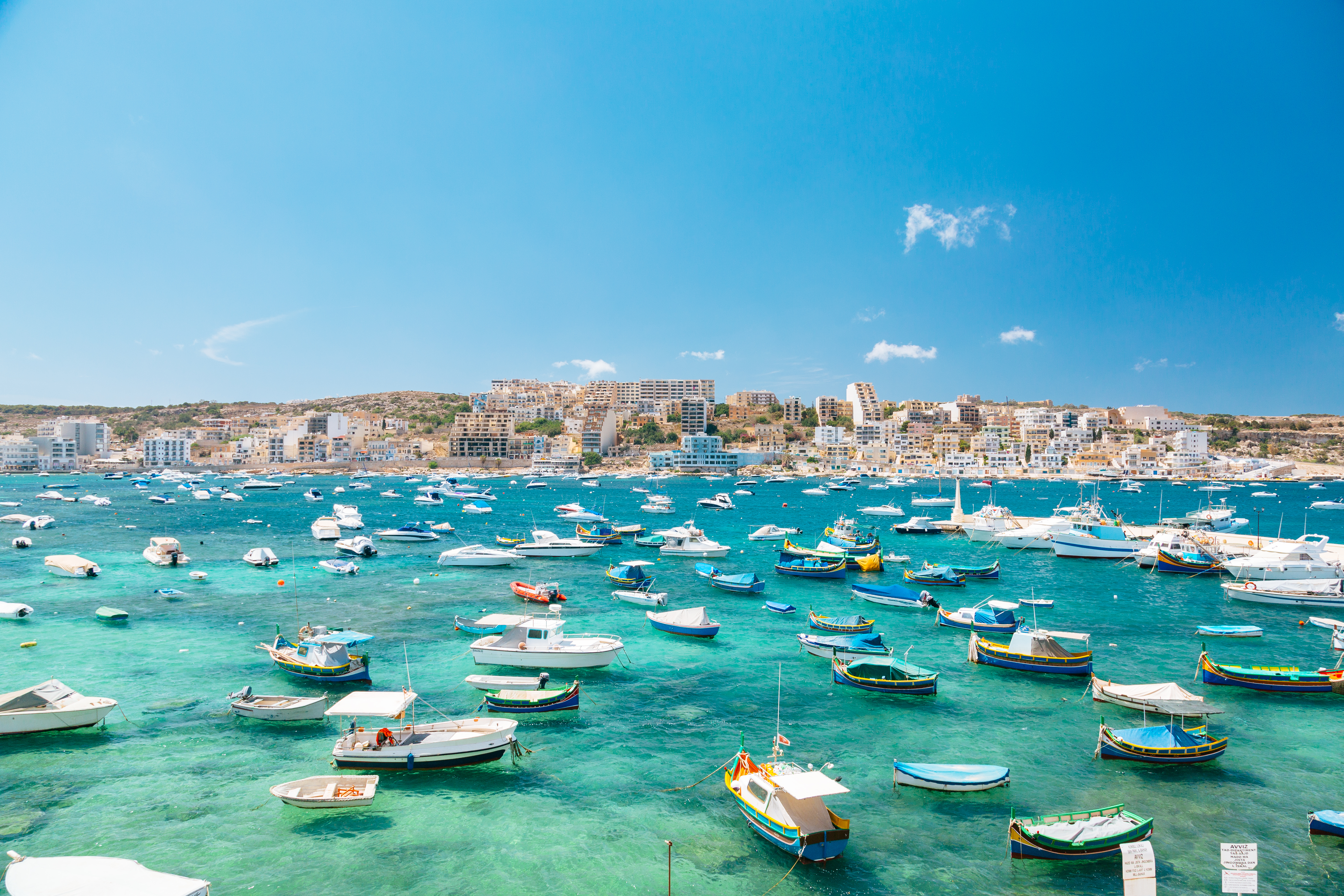 Marsaxlokk, Malta: luzzu coloridos y barcos en bahía de agua turquesa.