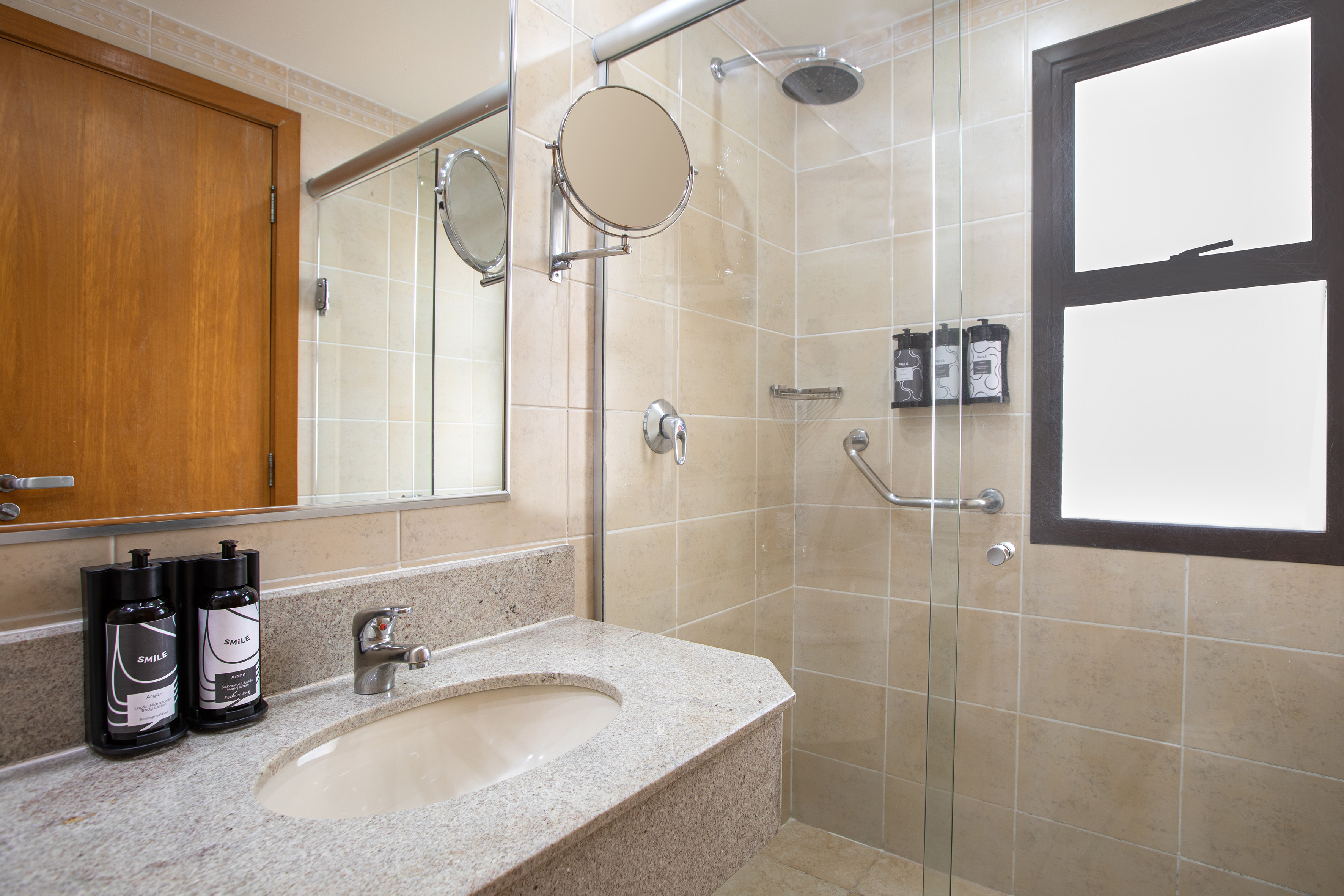 Modern tiled hotel bathroom with granite vanity, sink, and glass shower.