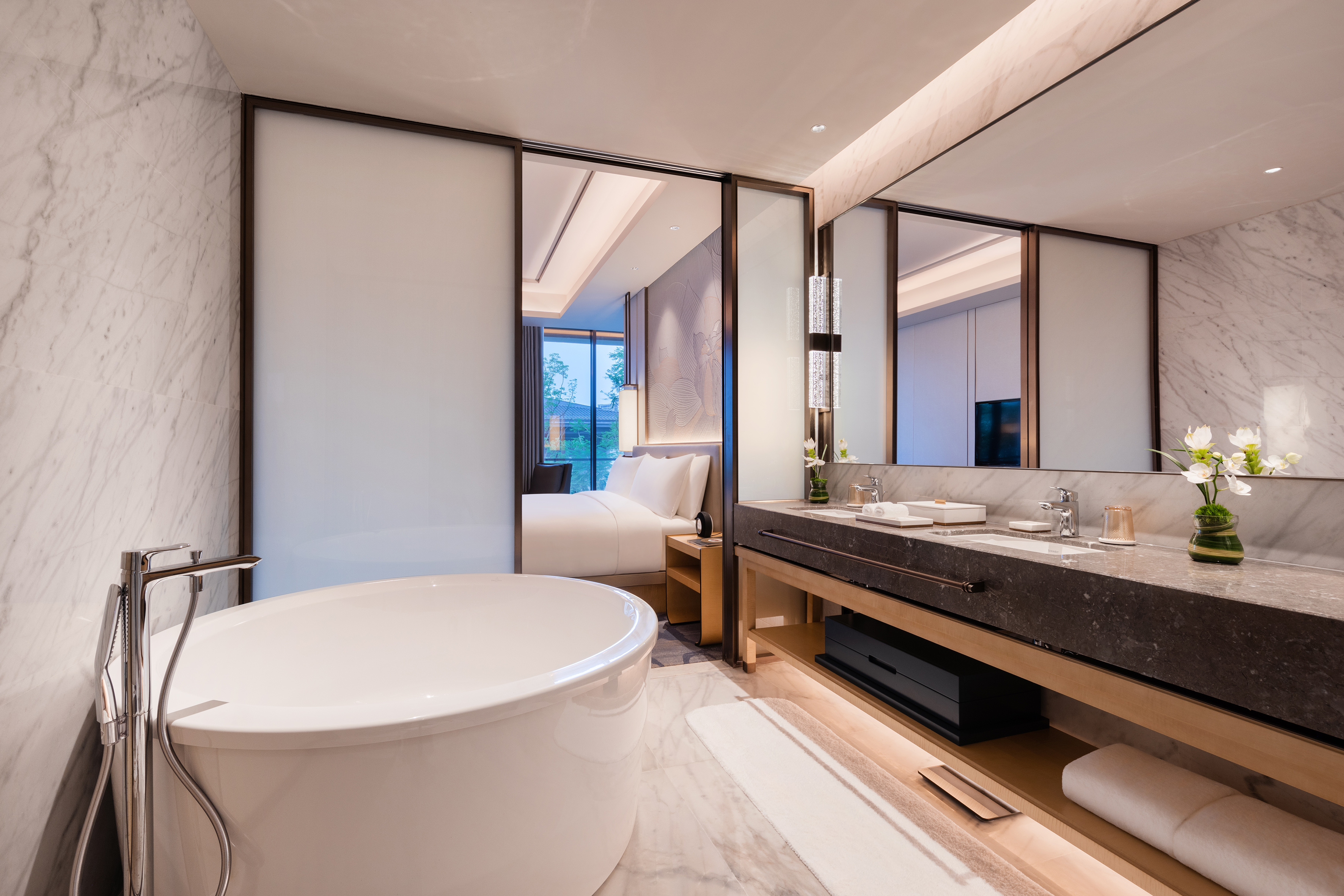 Modern luxury hotel bathroom with freestanding tub and vanity next to bedroom.