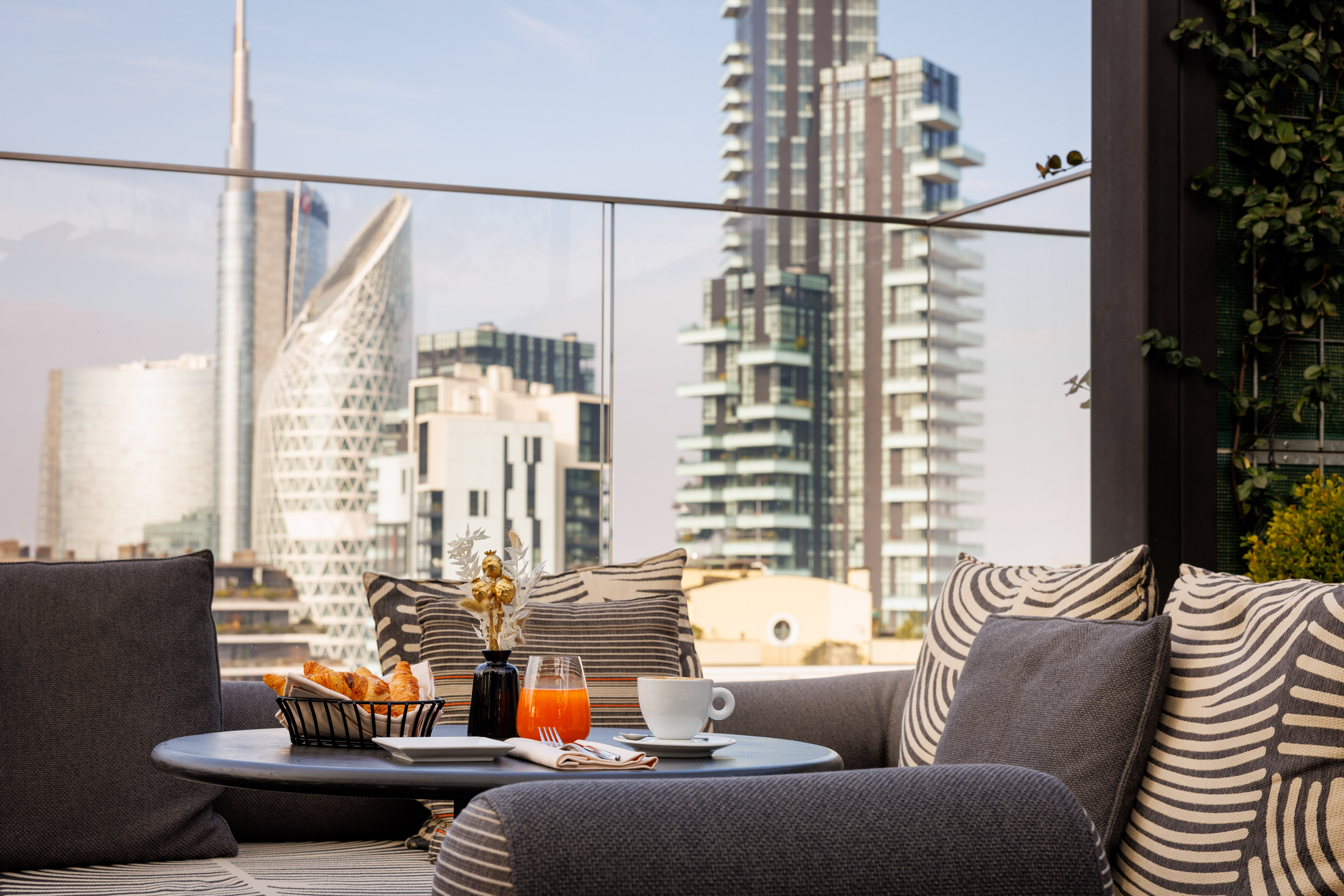 Terrace breakfast with croissants, coffee, and orange juice overlooking Milan skyline.