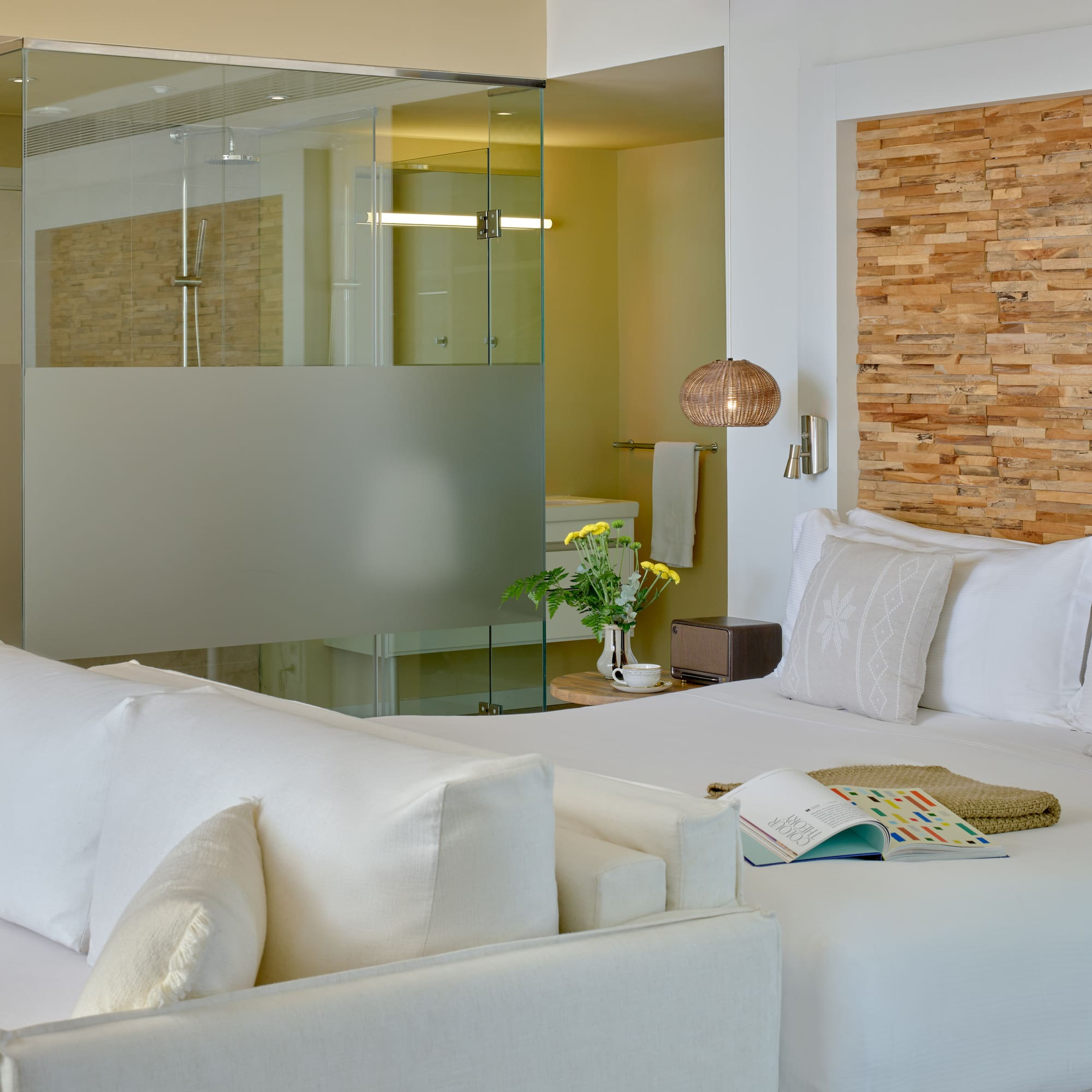 Modern hotel room with white bed, wood headboard, and glass shower.