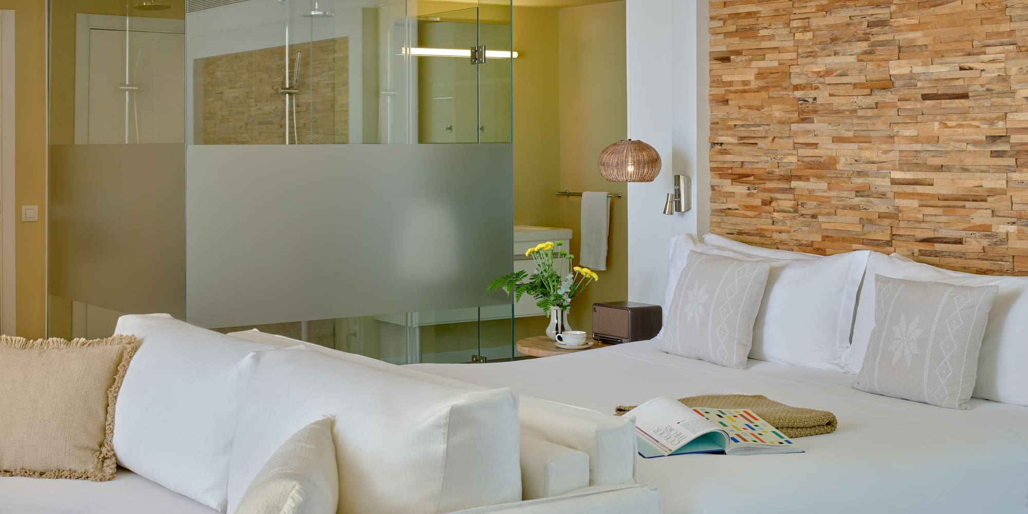 Modern hotel room with white bed, wood headboard, and glass shower.
