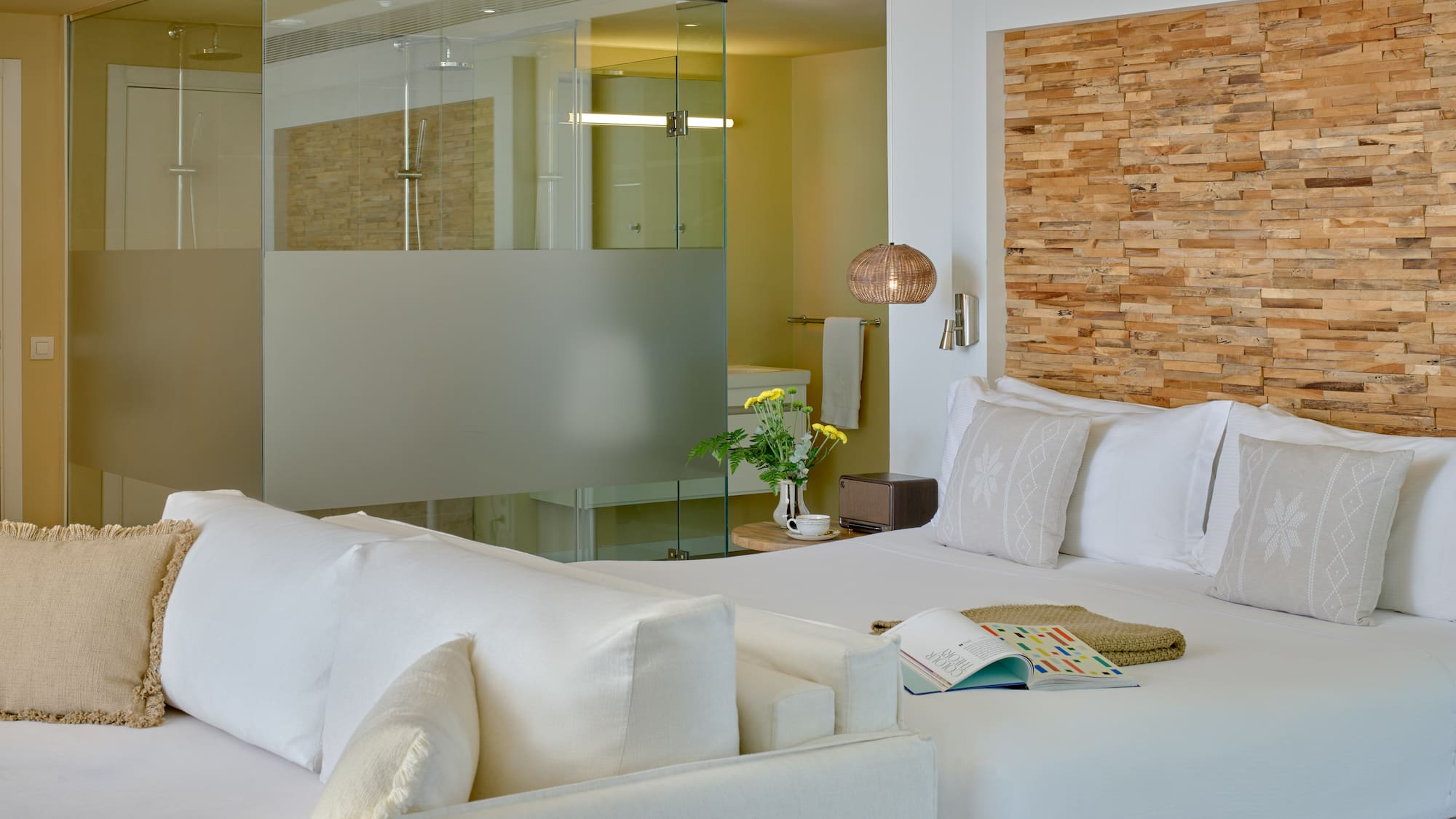 Modern hotel room with white bed, wood headboard, and glass shower.