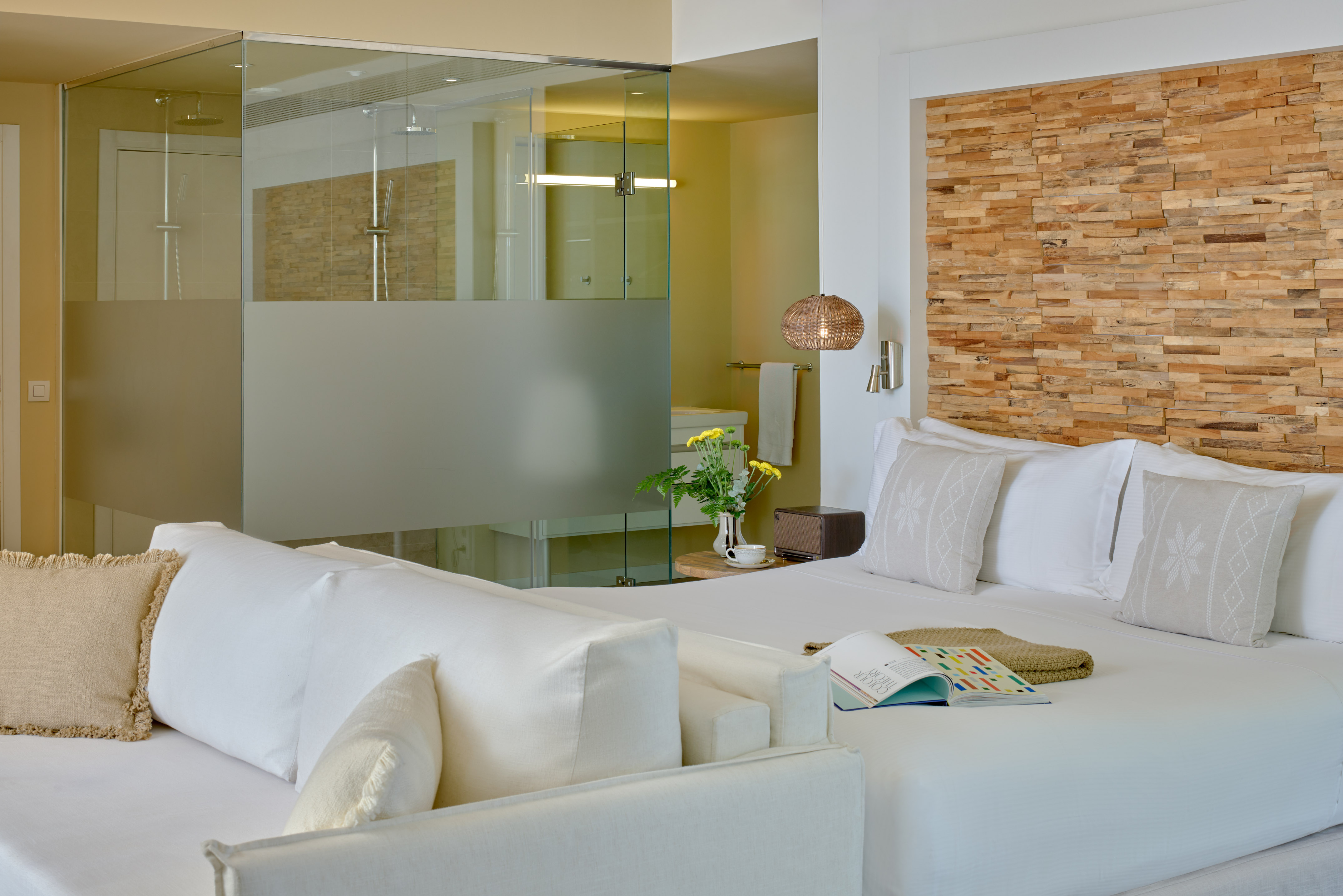 Modern hotel room with white bed, wood headboard, and glass shower.