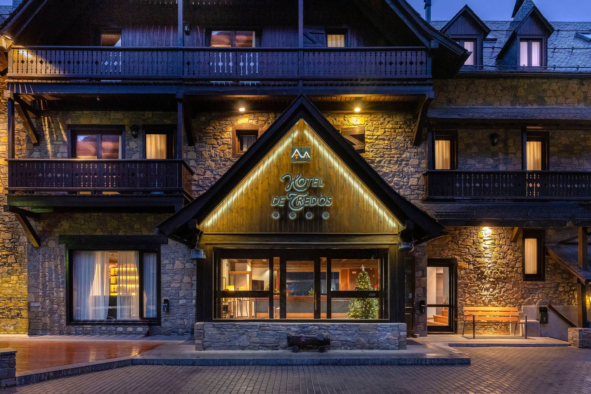 Illuminated Hotel de Tredos at night, stone and wood mountain architecture.