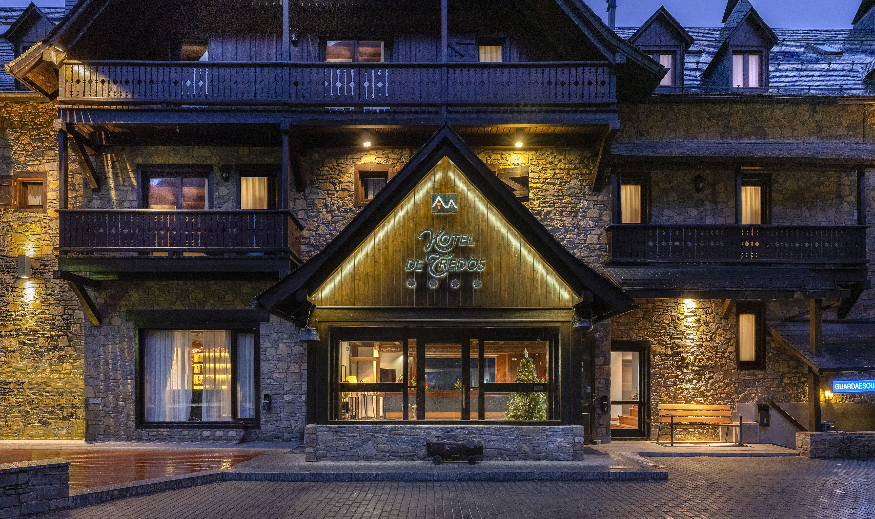 Illuminated Hotel de Tredos at night, stone and wood mountain architecture.