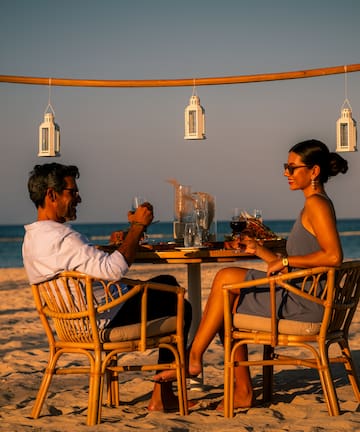 a man and woman sitting at a table on a beach