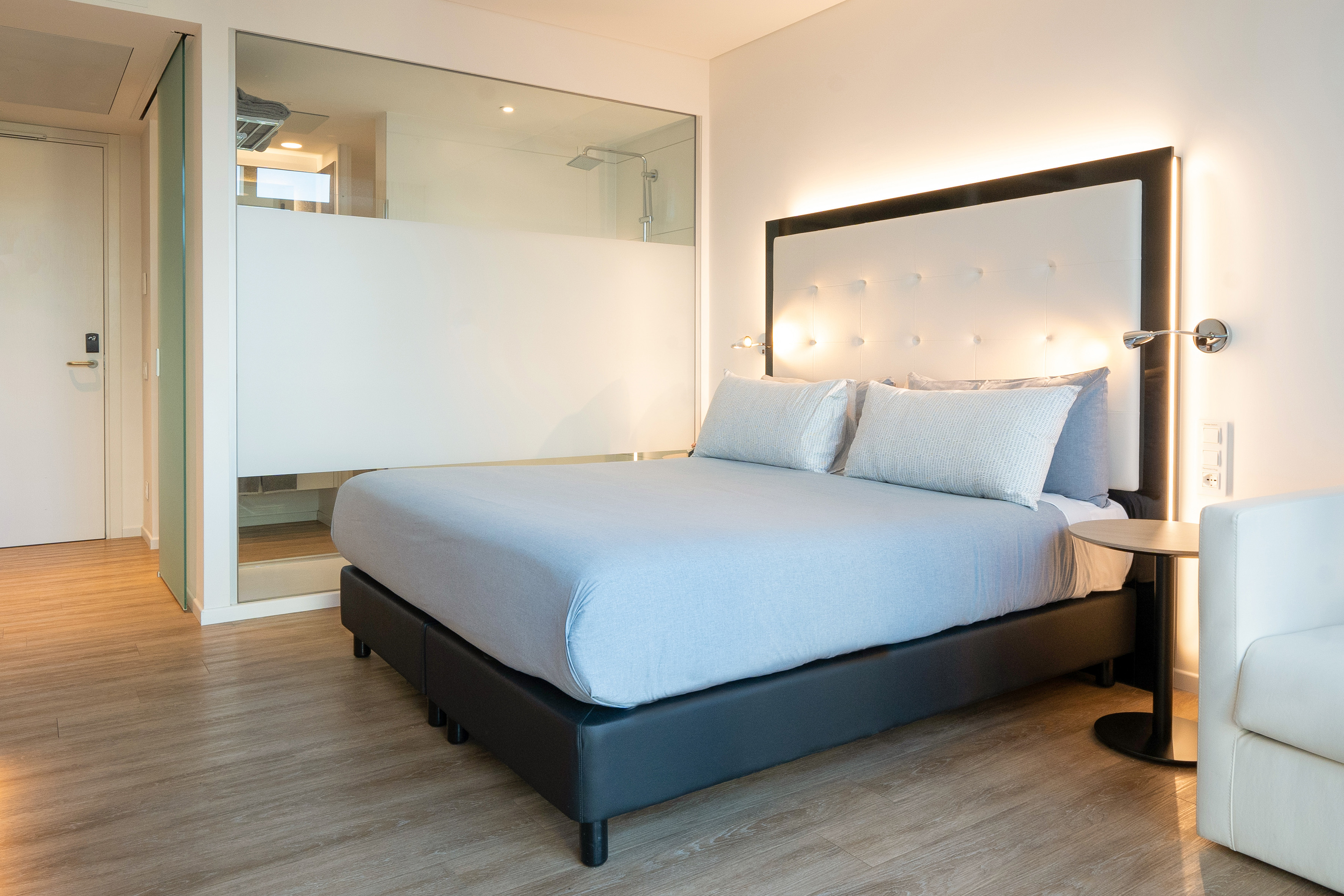 Bright modern hotel room with queen bed, backlit headboard, and glass shower.