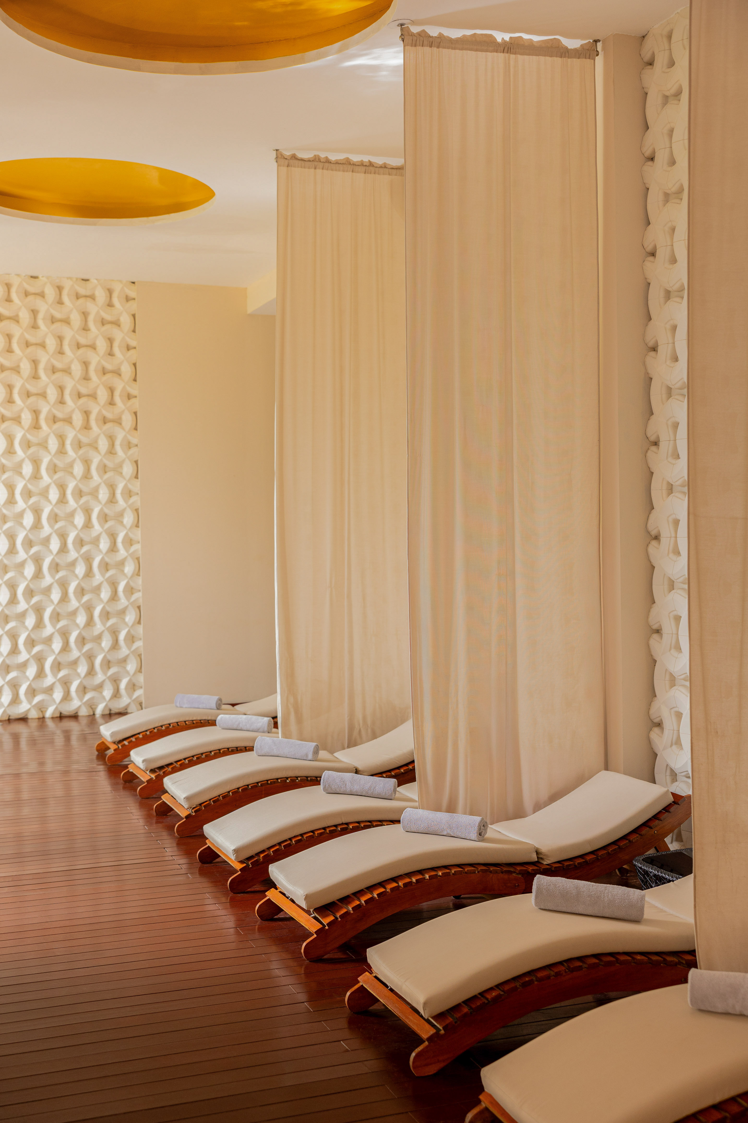 Row of spa loungers with towels and privacy curtains in a tranquil relaxation area.