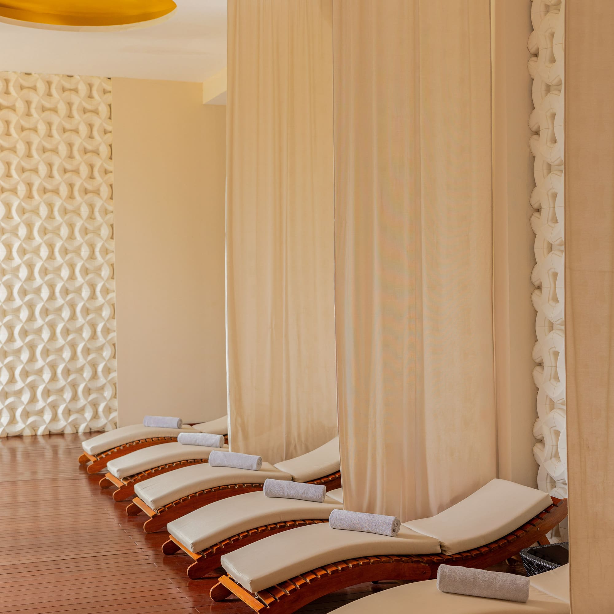 Row of spa loungers with towels and privacy curtains in a tranquil relaxation area.