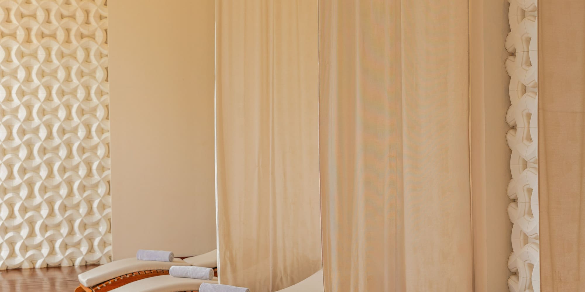 Row of spa loungers with towels and privacy curtains in a tranquil relaxation area.