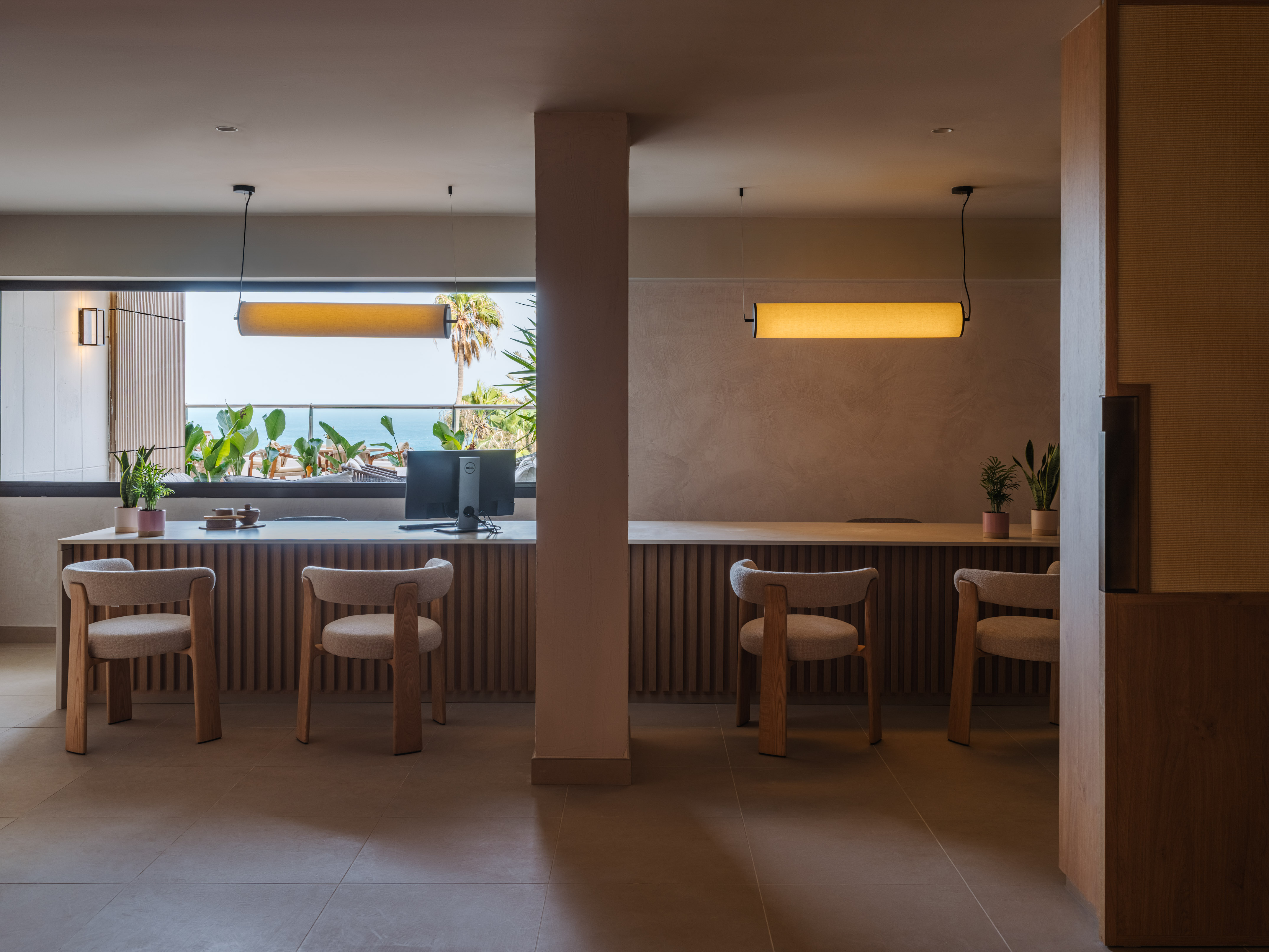 Modern hotel reception desk with wood details, two chairs, and ocean view.