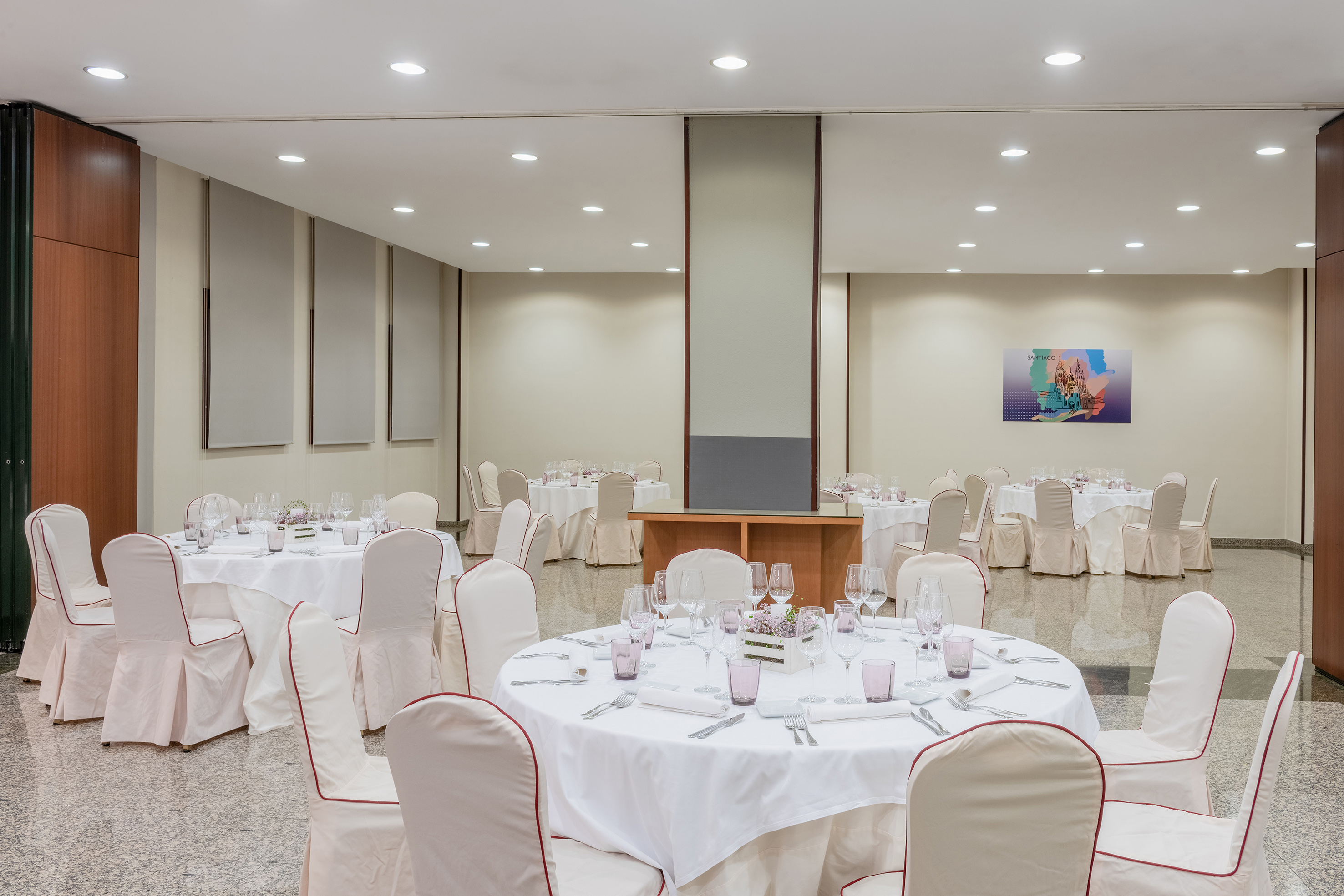 Banquet hall setup with white round tables and red-trimmed chairs for an event.