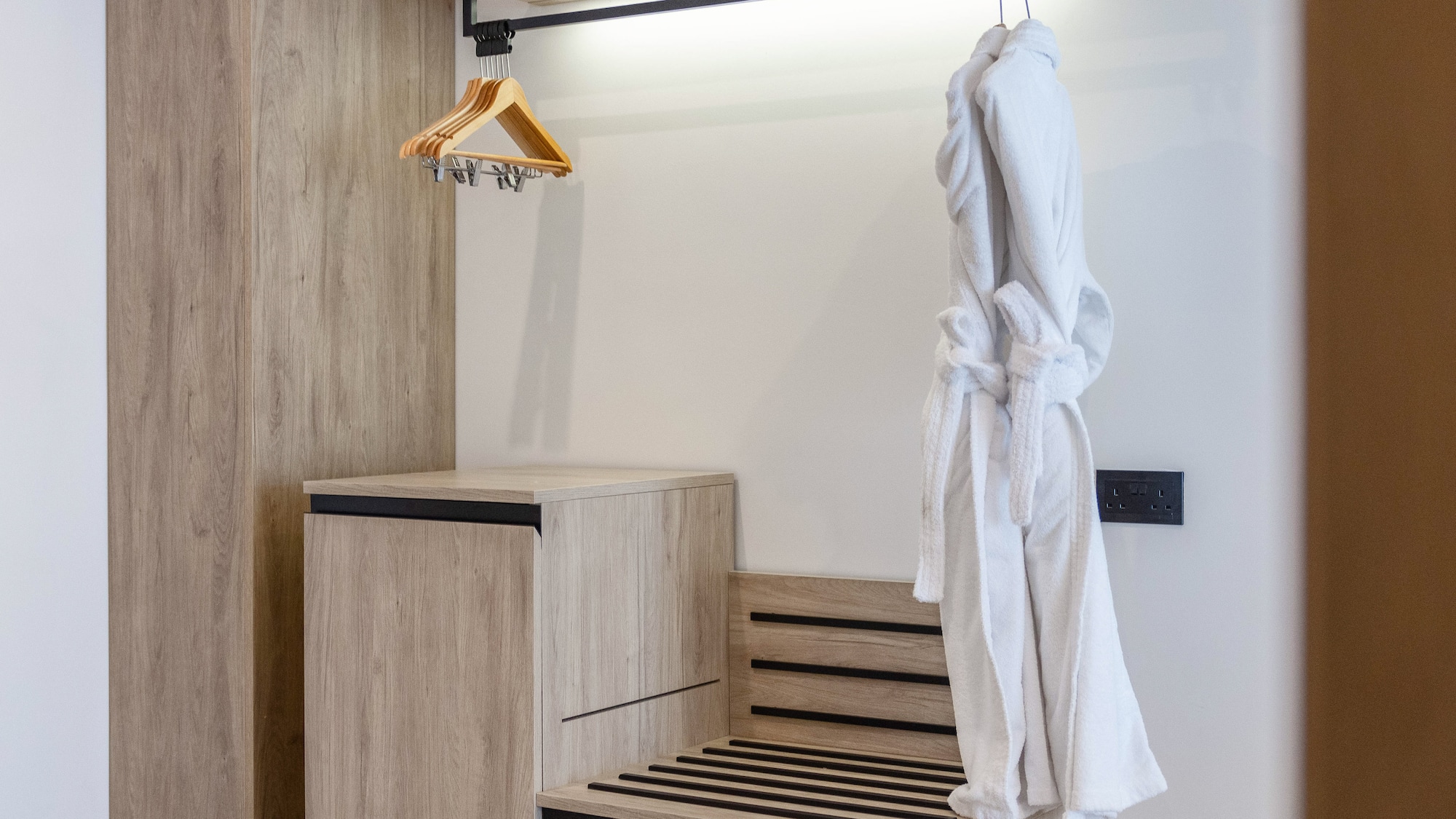 Modern hotel wardrobe with integrated luggage rack and white bathrobe.