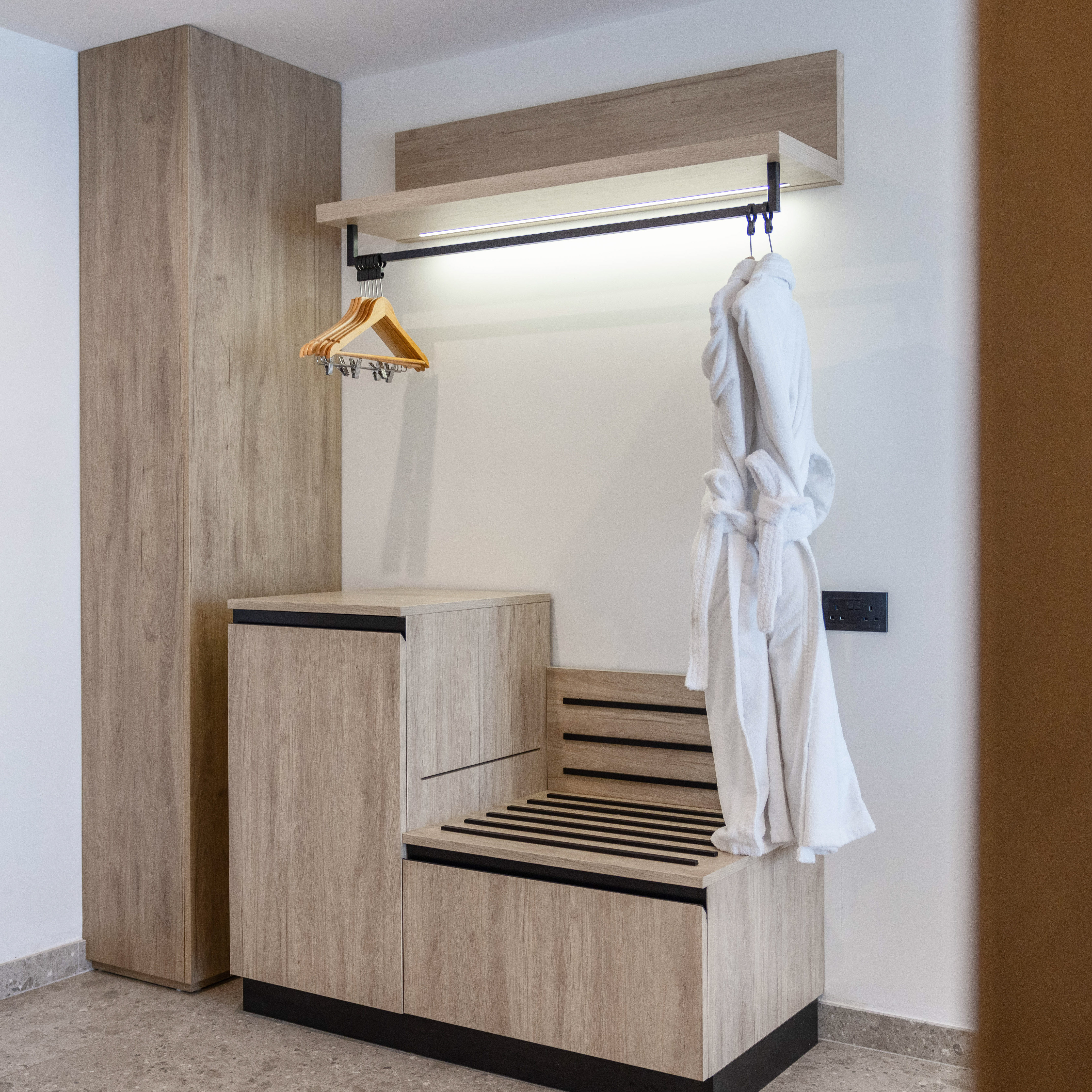 Modern hotel wardrobe with integrated luggage rack and white bathrobe.