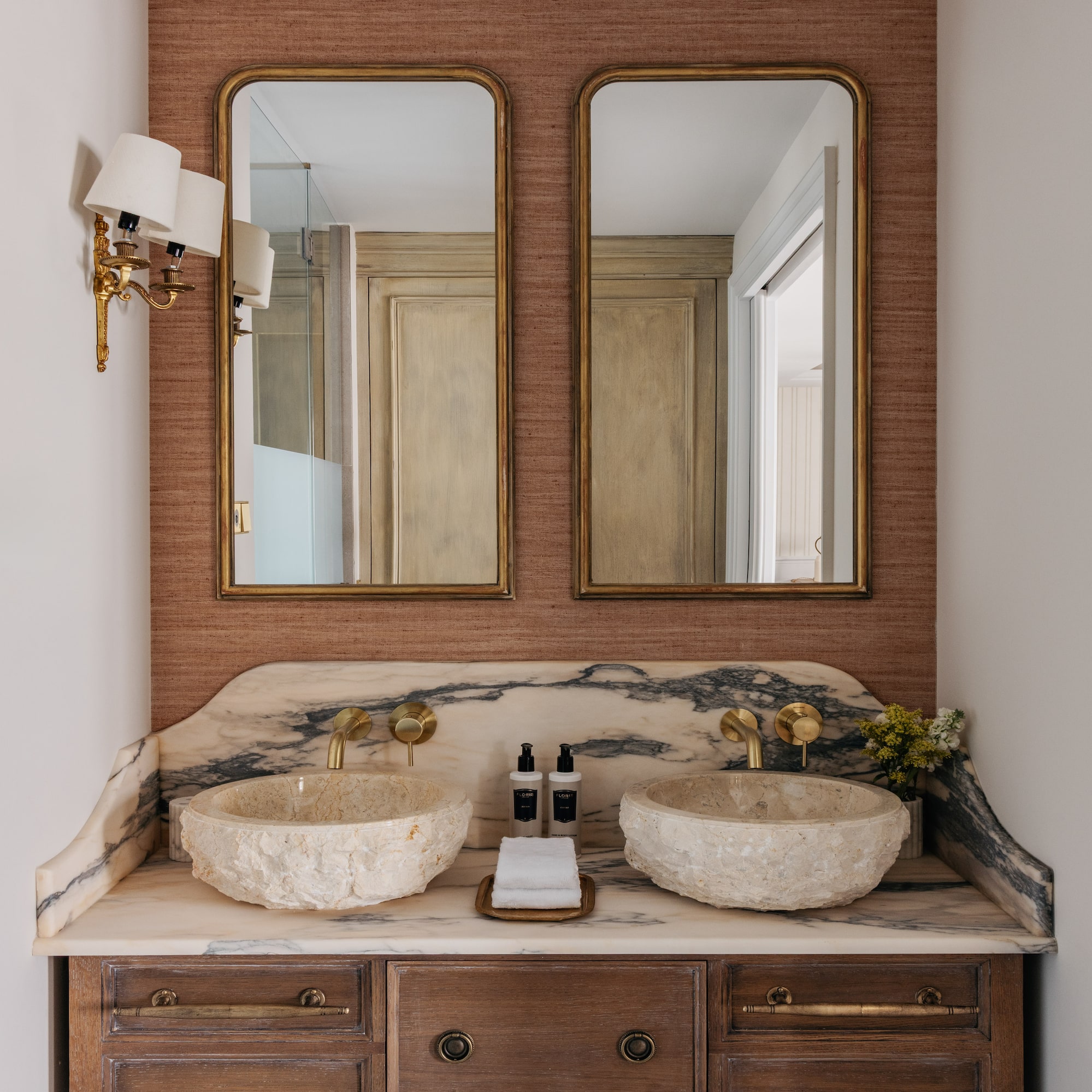 Luxury dual vanity bathroom with stone sinks, marble counter, and gold mirrors.
