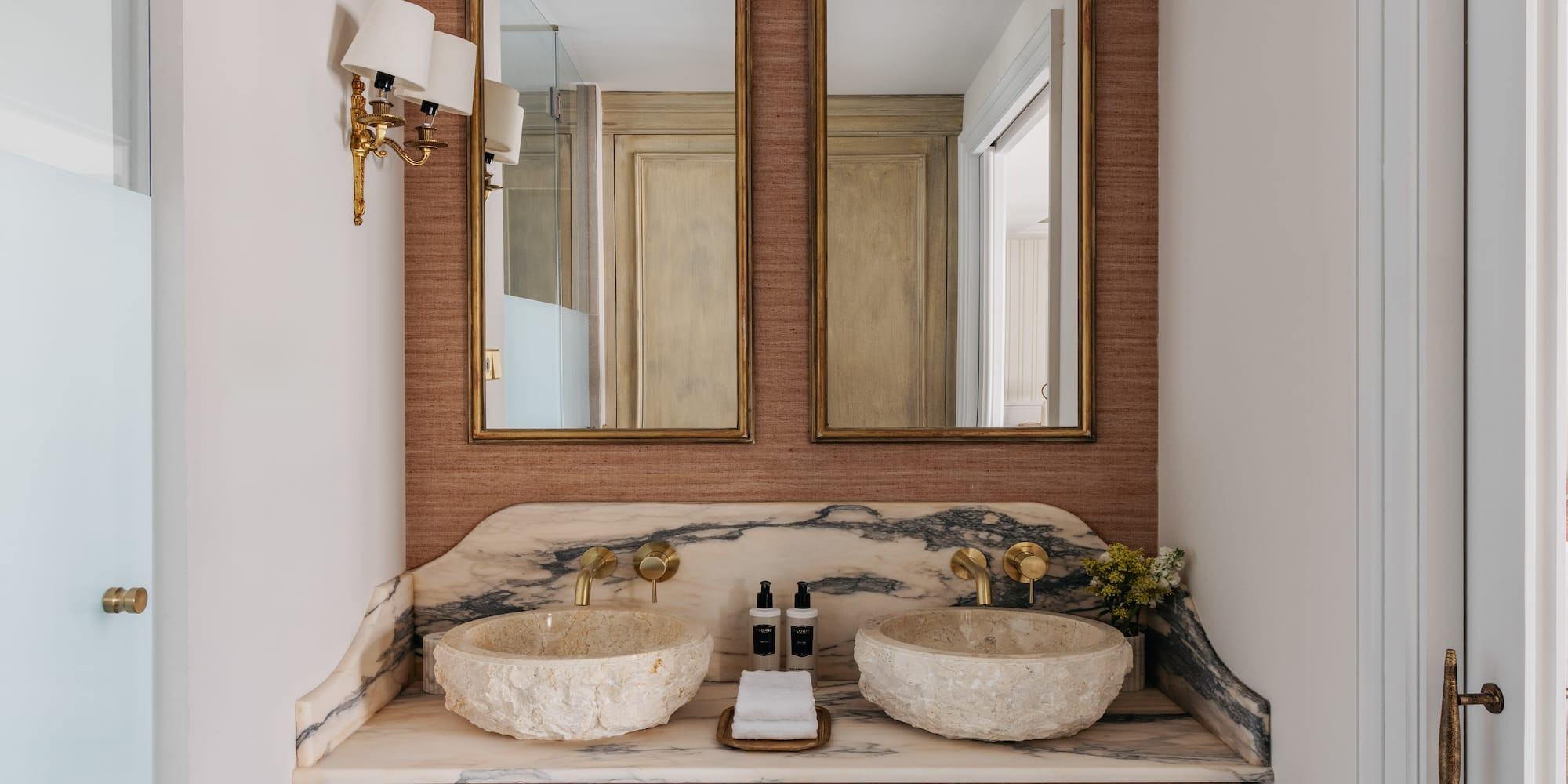 Luxury dual vanity bathroom with stone sinks, marble counter, and gold mirrors.