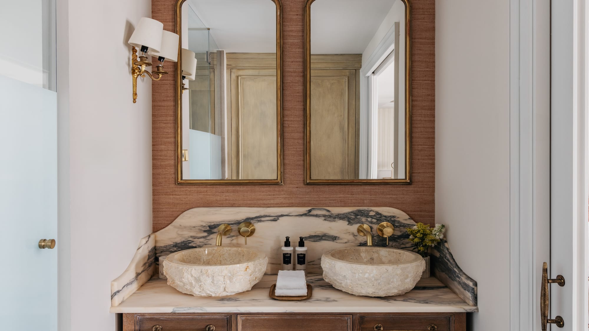 Luxury dual vanity bathroom with stone sinks, marble counter, and gold mirrors.