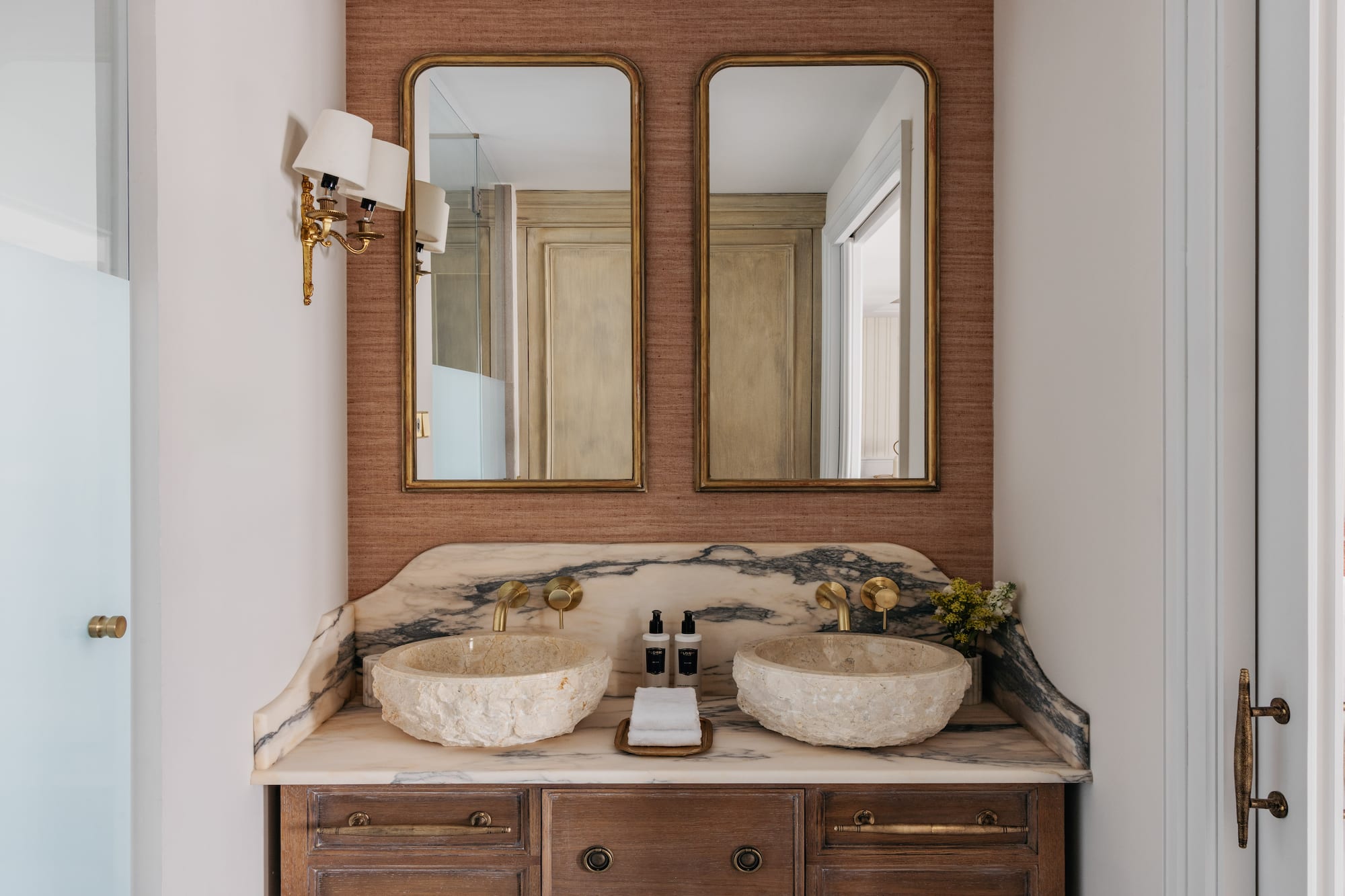 Luxury dual vanity bathroom with stone sinks, marble counter, and gold mirrors.