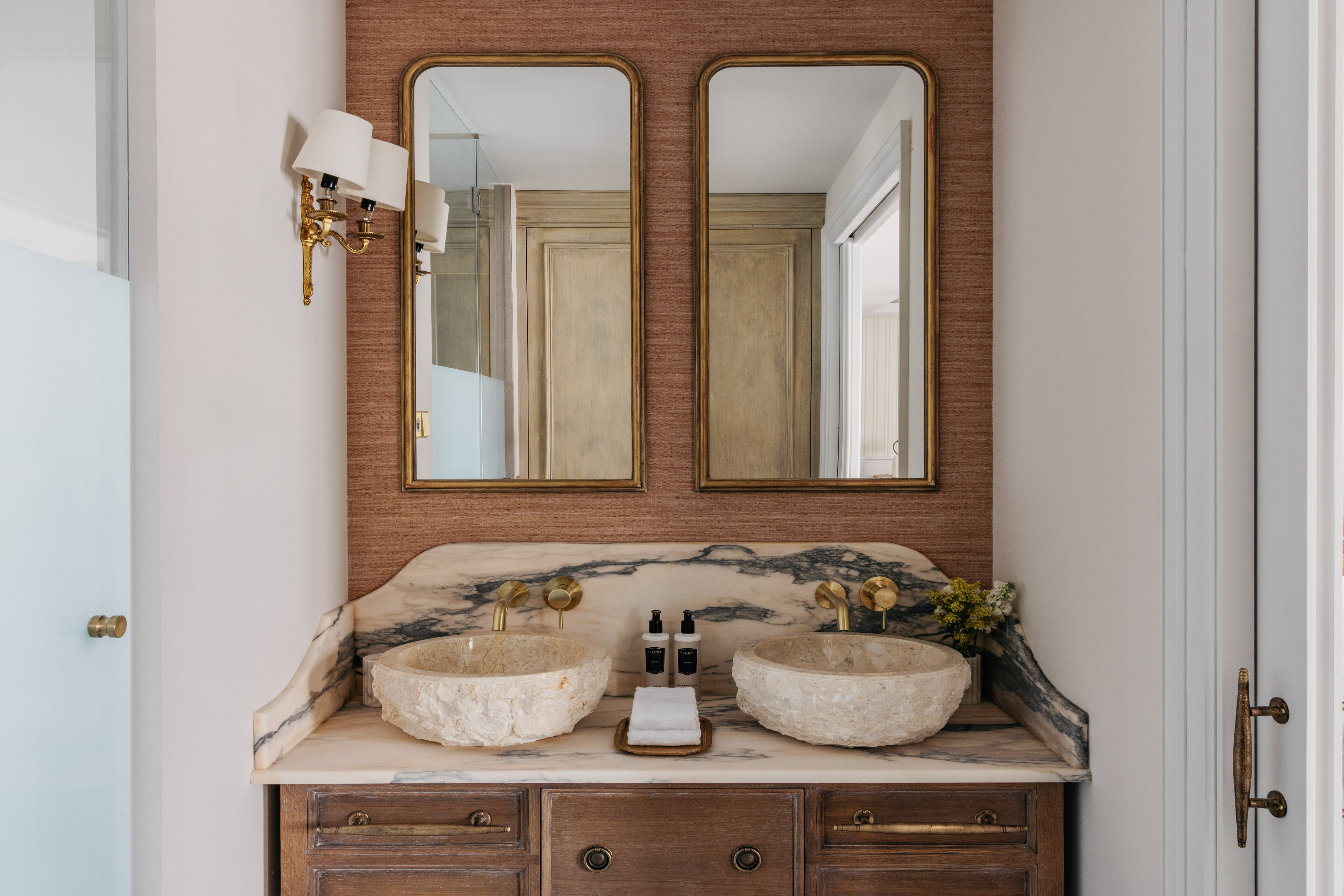 Luxury dual vanity bathroom with stone sinks, marble counter, and gold mirrors.