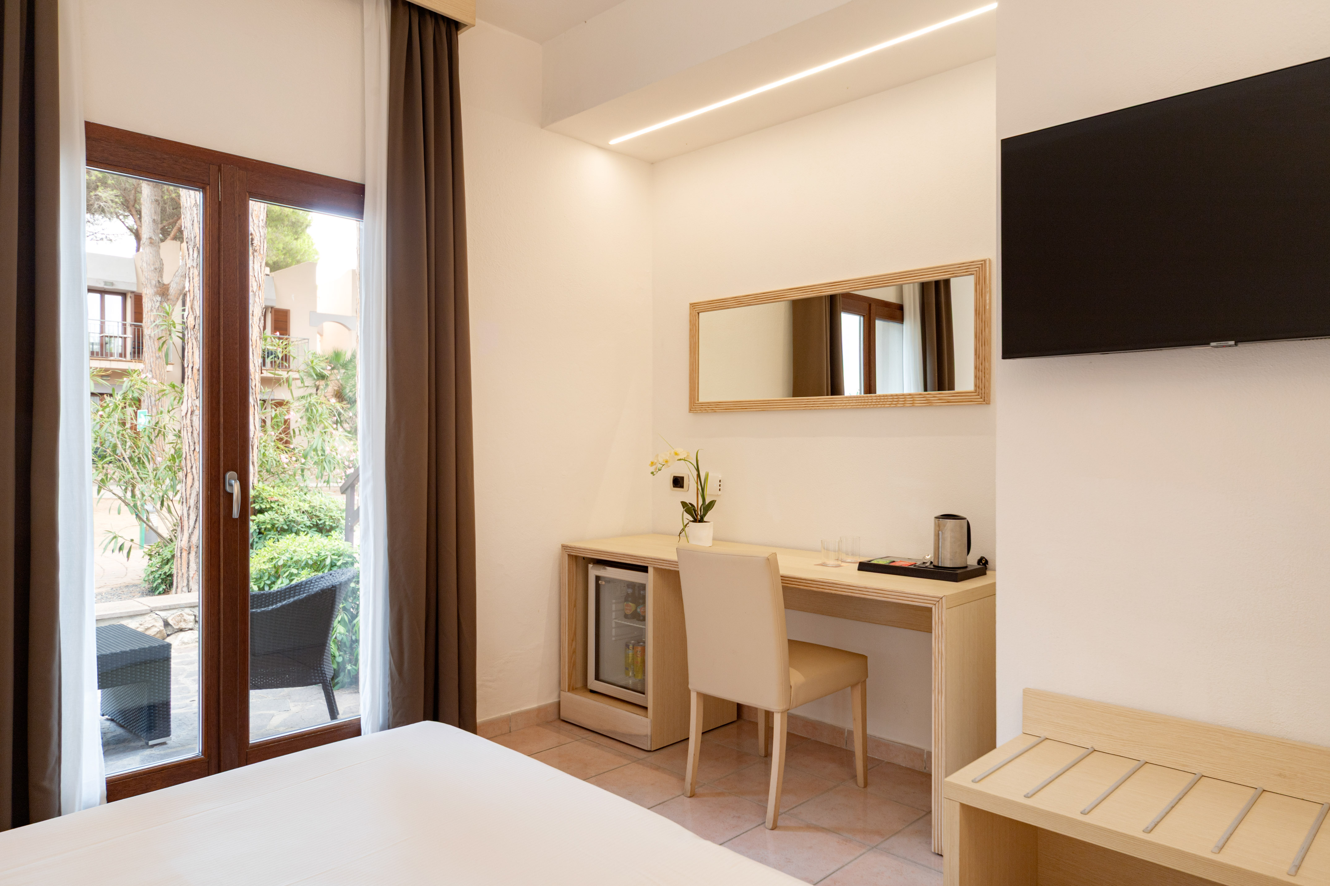 Modern hotel bedroom with desk, mini-fridge, wall TV, and patio view.