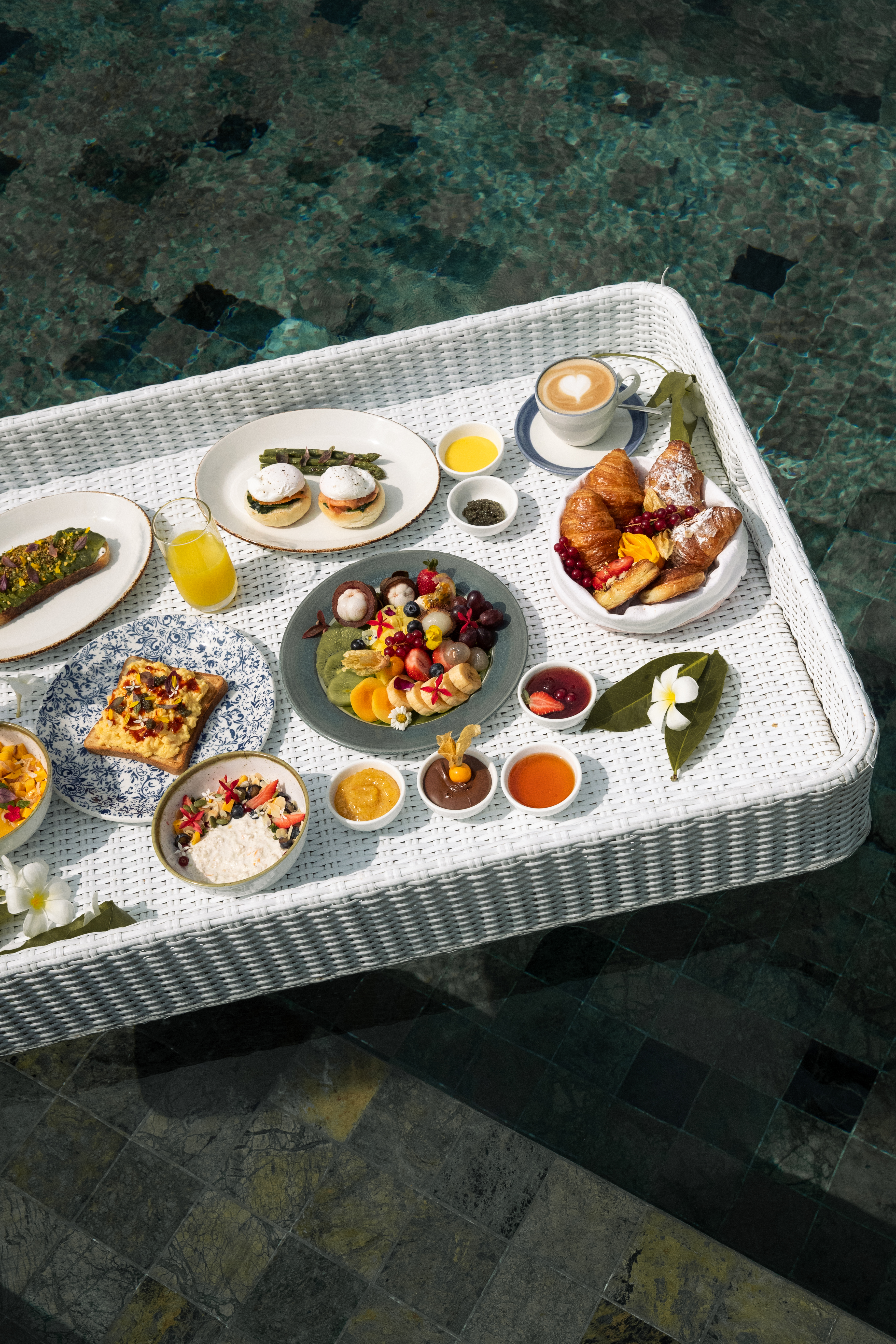 Luxury floating breakfast in pool with fruit, pastries, coffee, and eggs.