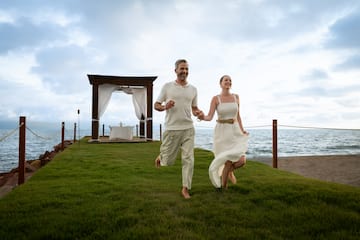 a man and woman running on grass by the ocean