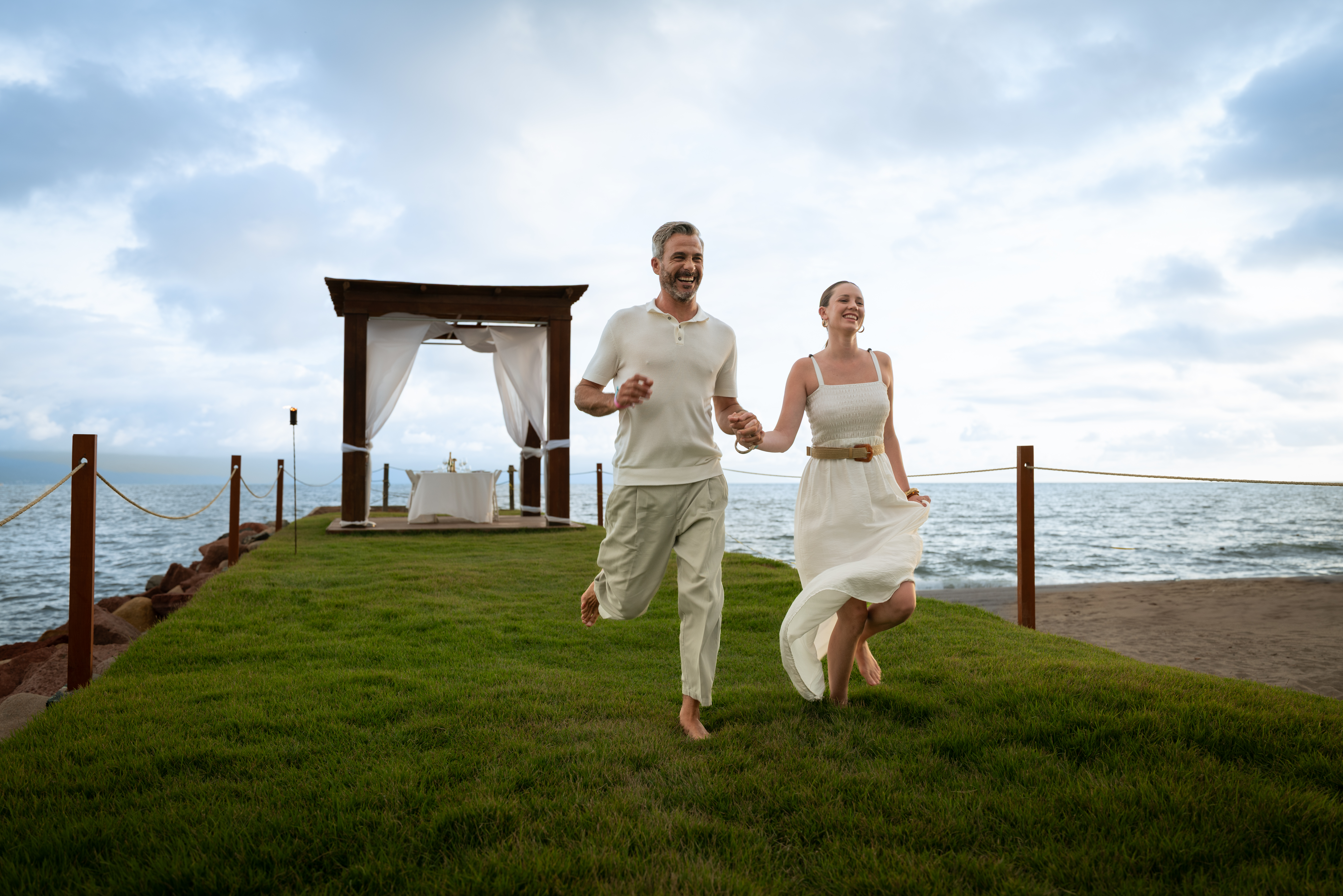 a man and woman running on grass by the ocean