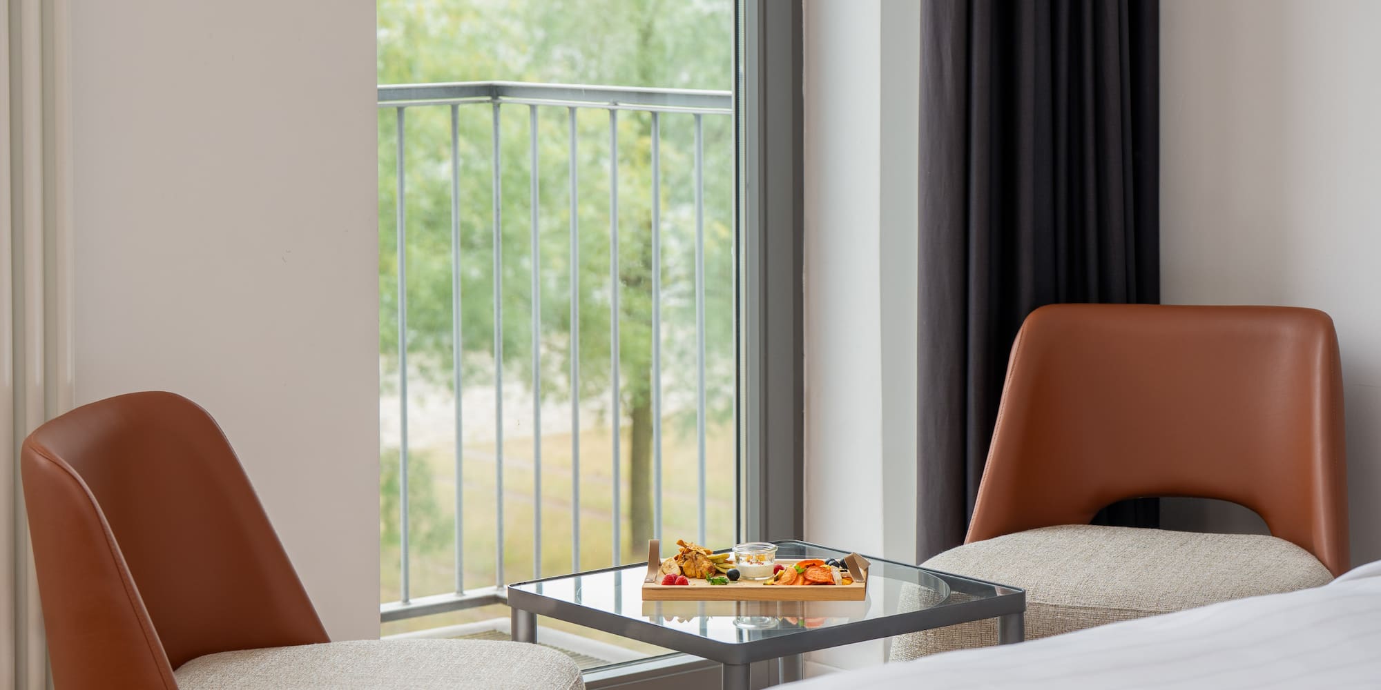 a tray of food on a glass table next to a bed and chairs