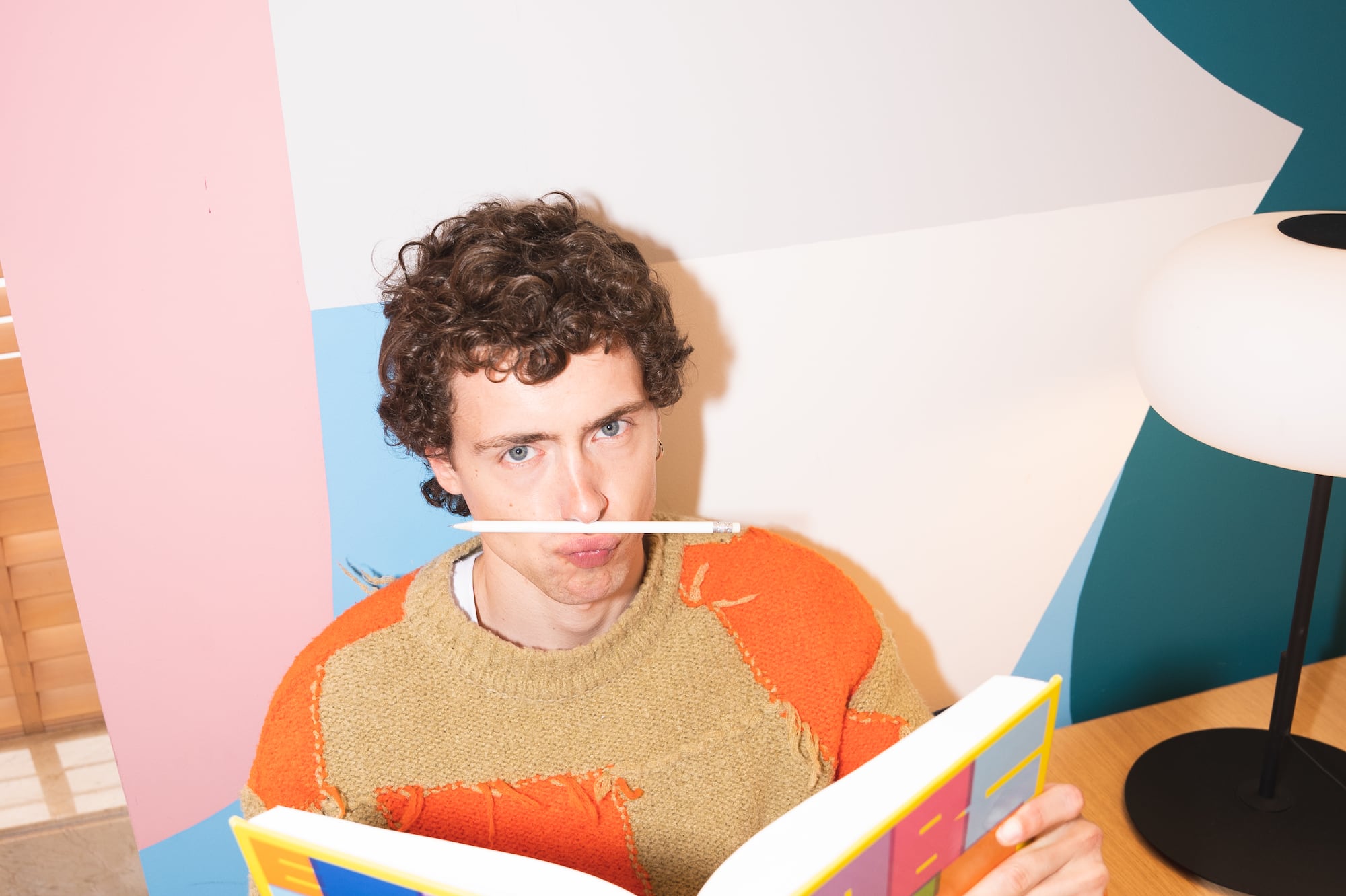 a man sitting at a table with a book and a pencil in his mouth
