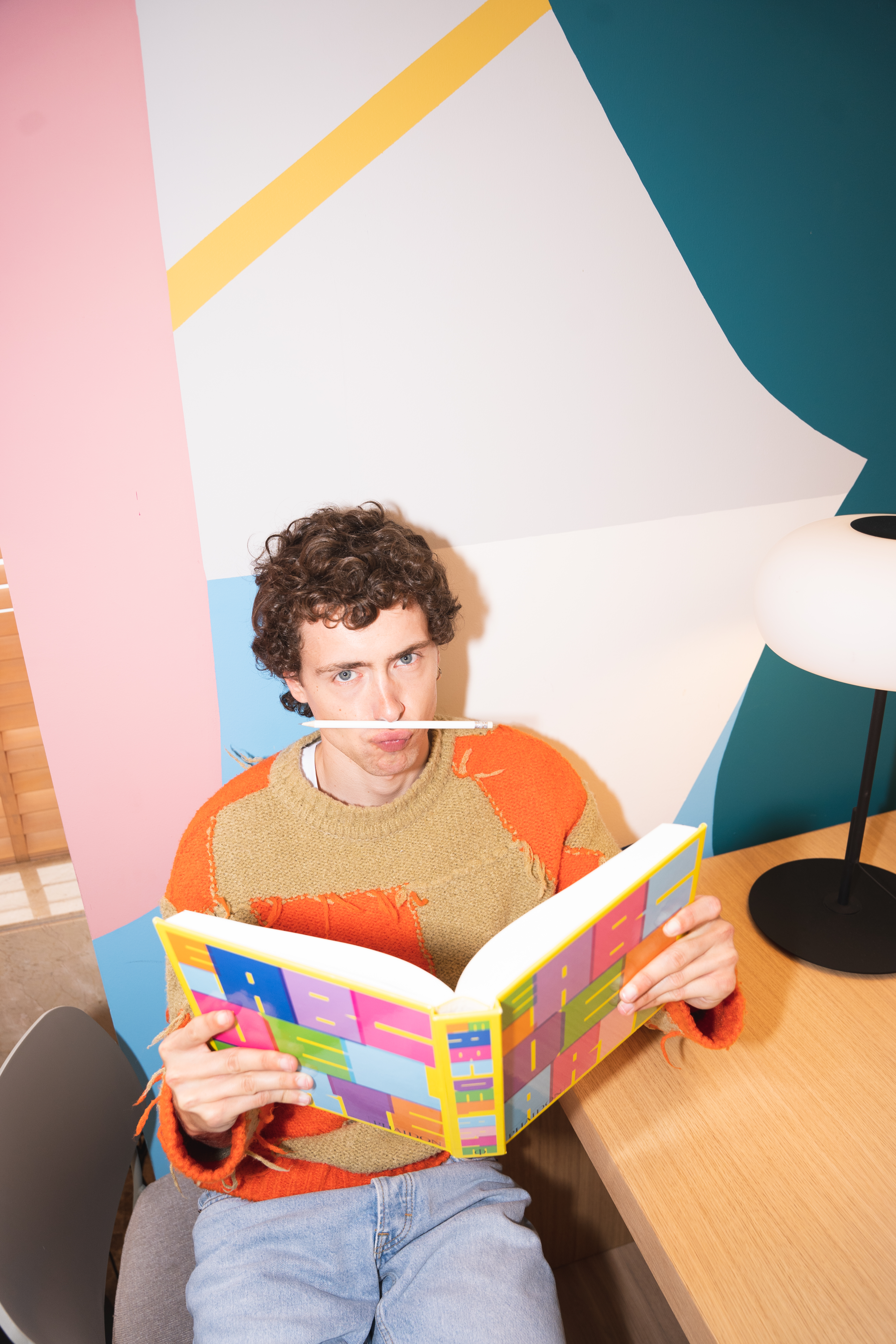 a man sitting at a table with a book and a pencil in his mouth
