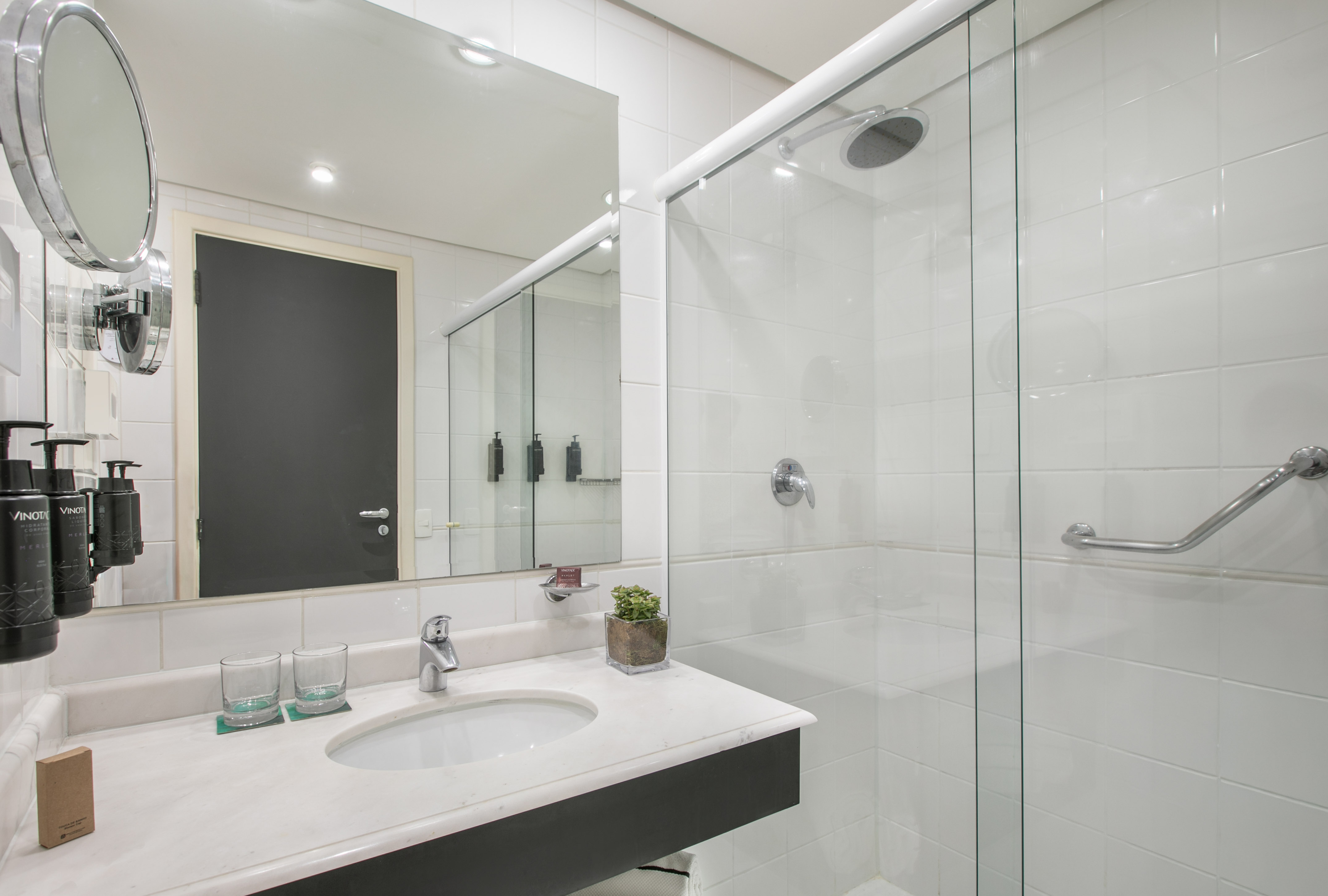 Modern white tiled bathroom with vanity, mirror, and glass shower.