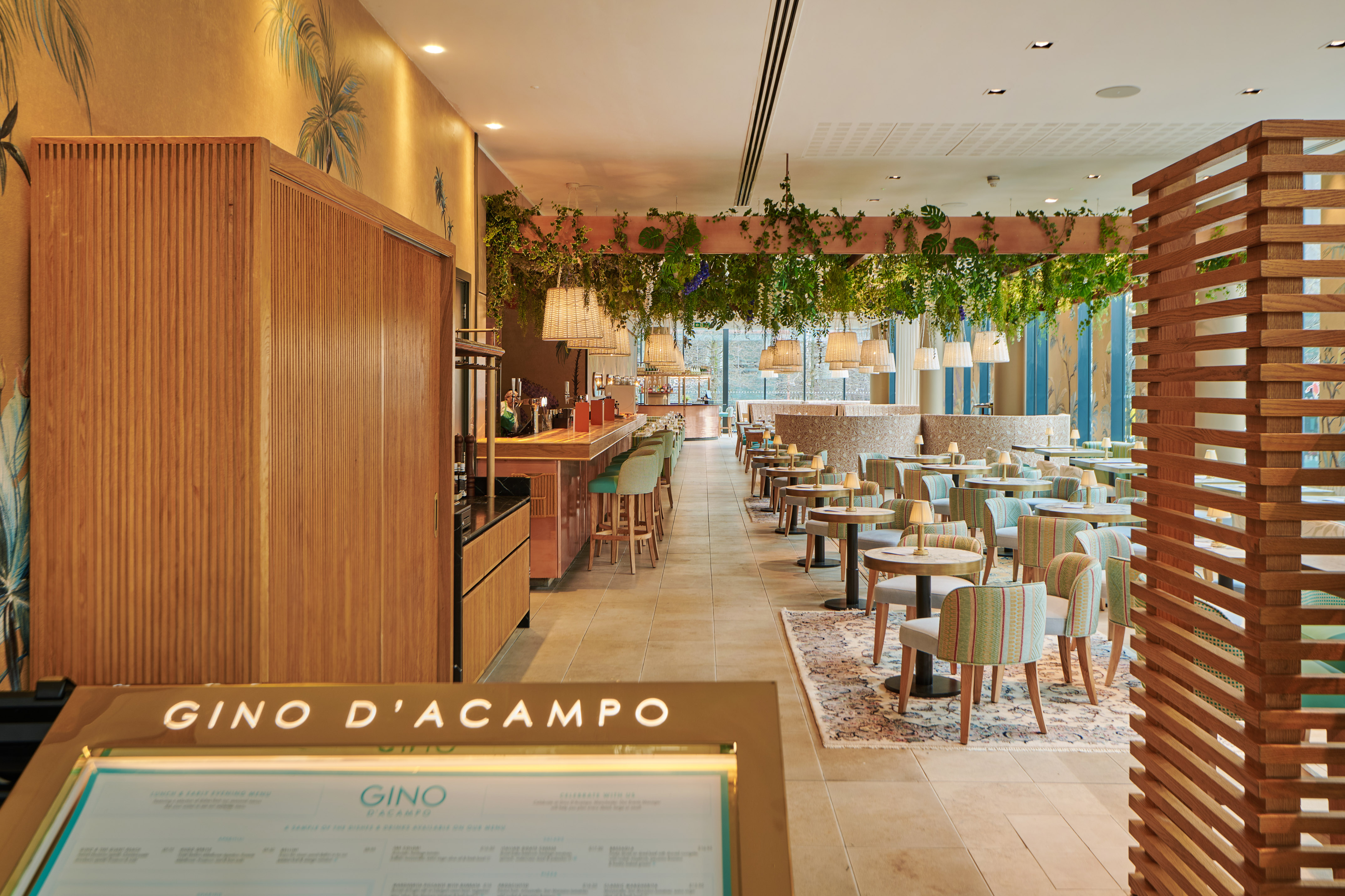 Gino D'Acampo restaurant interior: modern dining, bar, lush hanging plants.