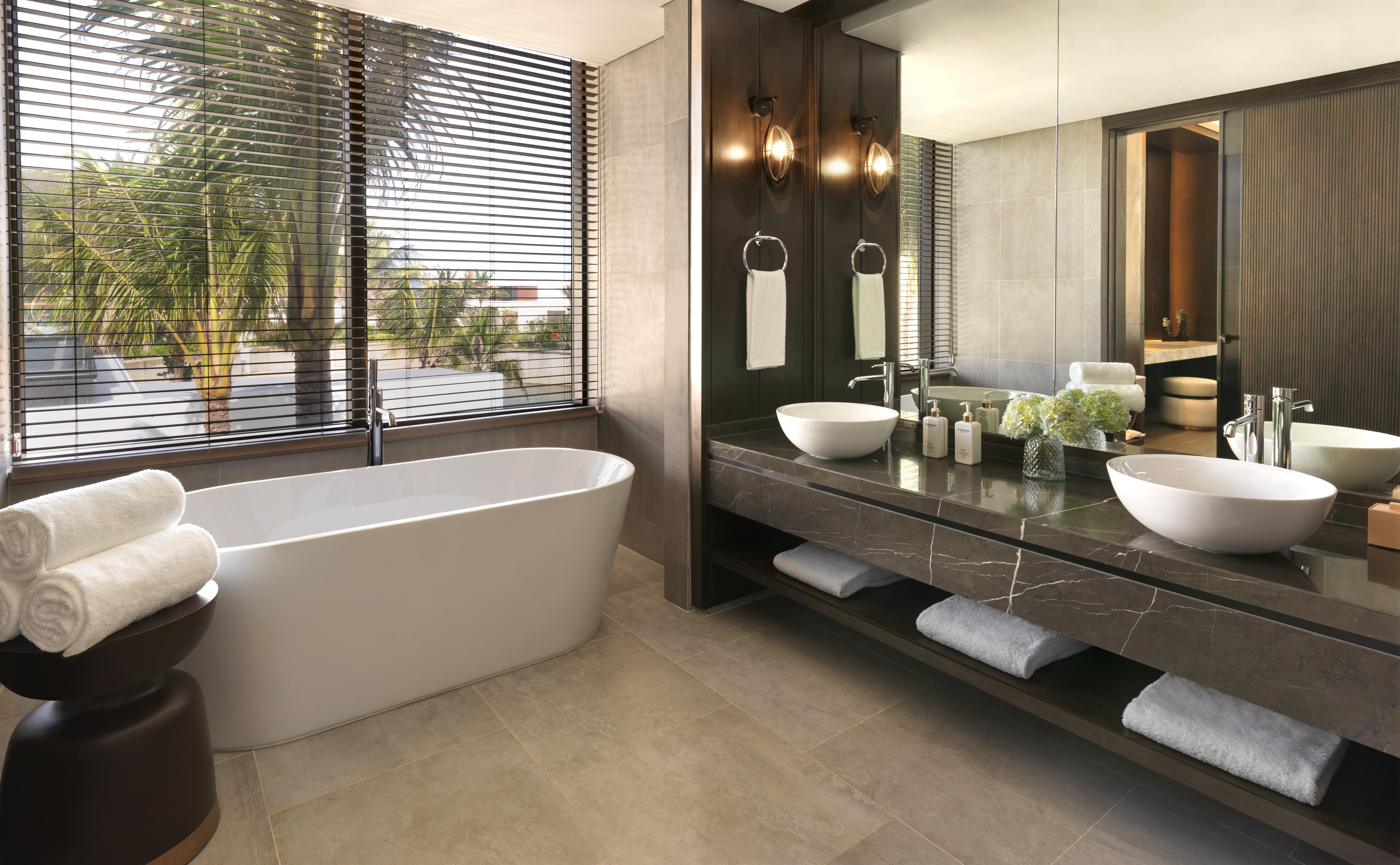 Modern luxury bathroom with freestanding tub, double vanity, and palm tree view.