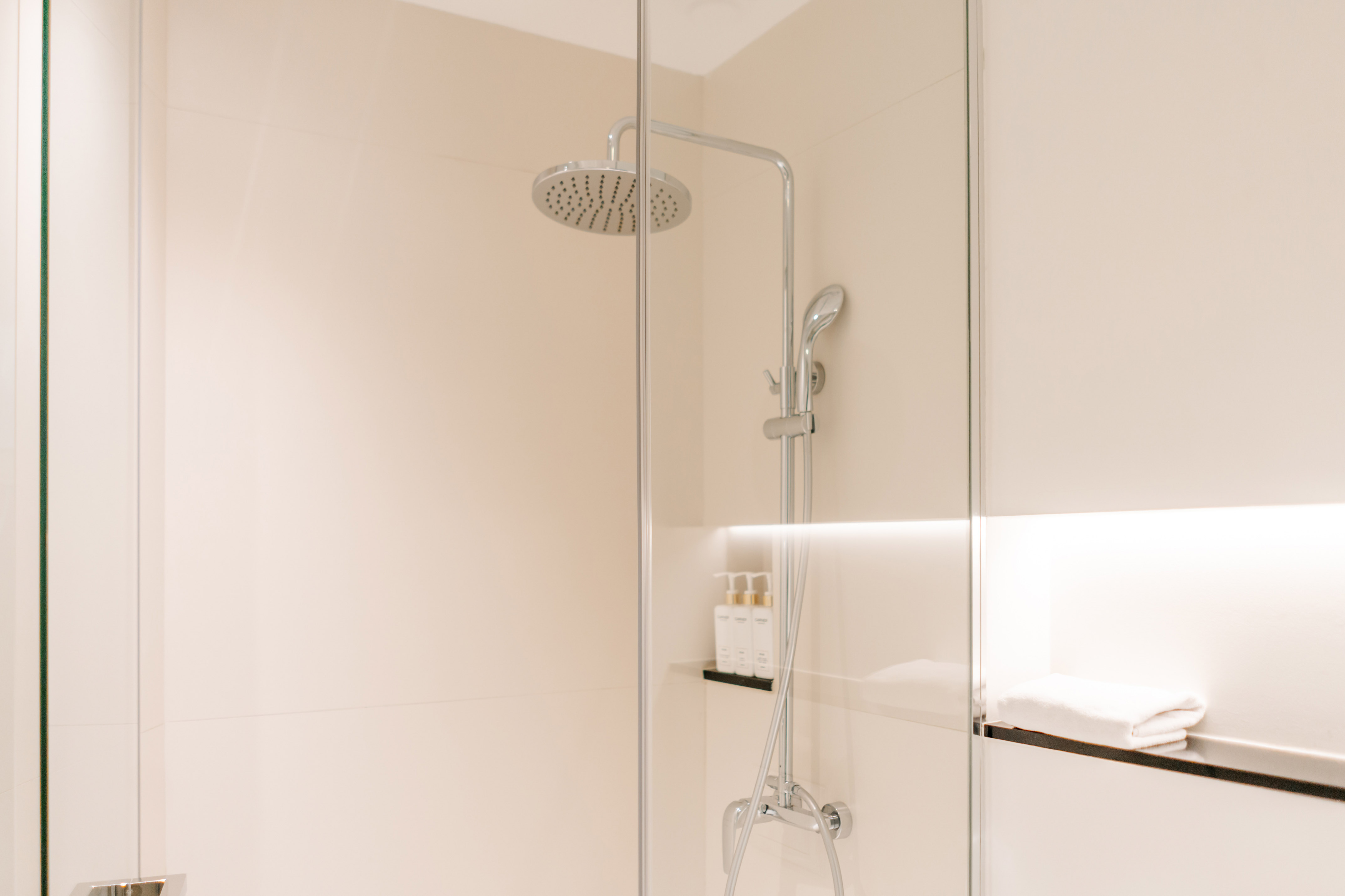 Modern bathroom shower with glass partition, rain head, toiletries, and towel.