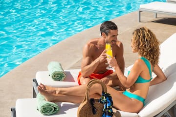 a man and woman sitting on a lounge chair by a pool
