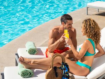 a man and woman sitting on a lounge chair by a pool