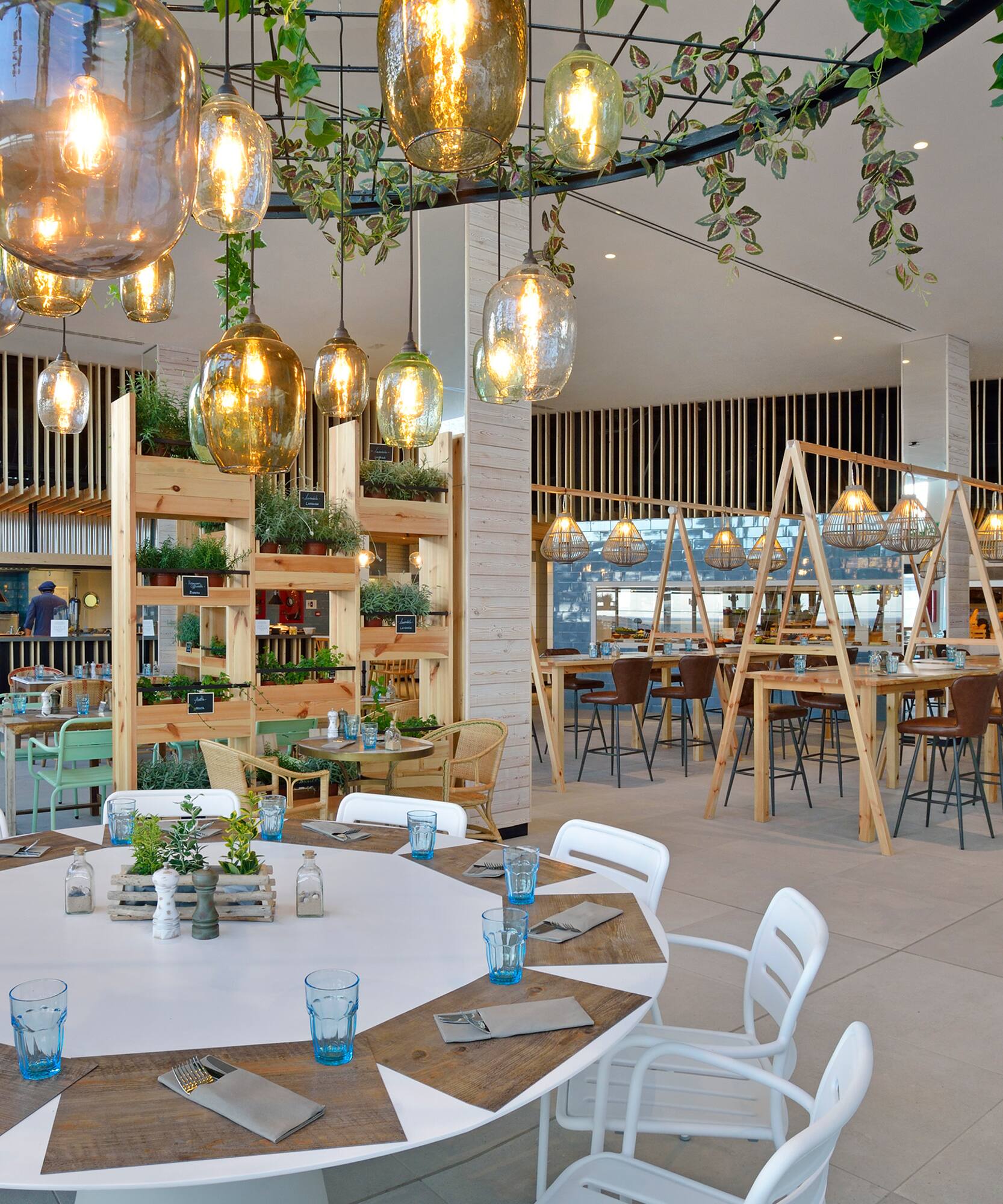 Contemporary restaurant with herbal decor, hanging lights, and open kitchen.