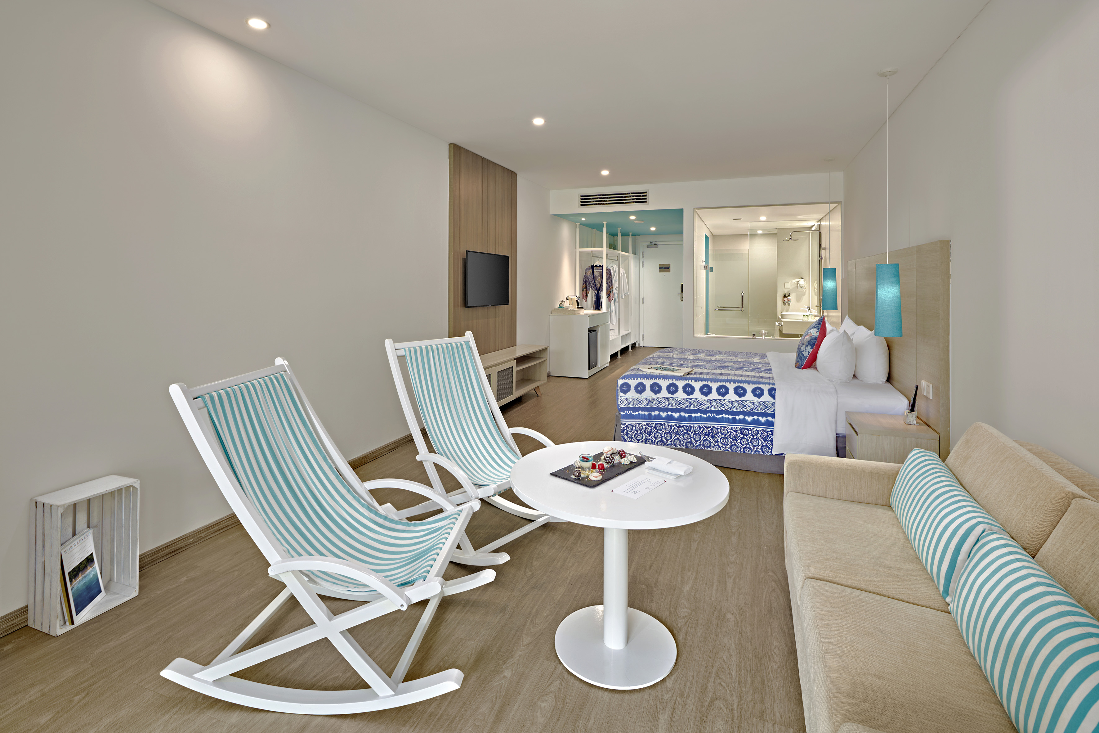 Modern hotel room with blue-white bed, sofa, and striped rocking chairs.