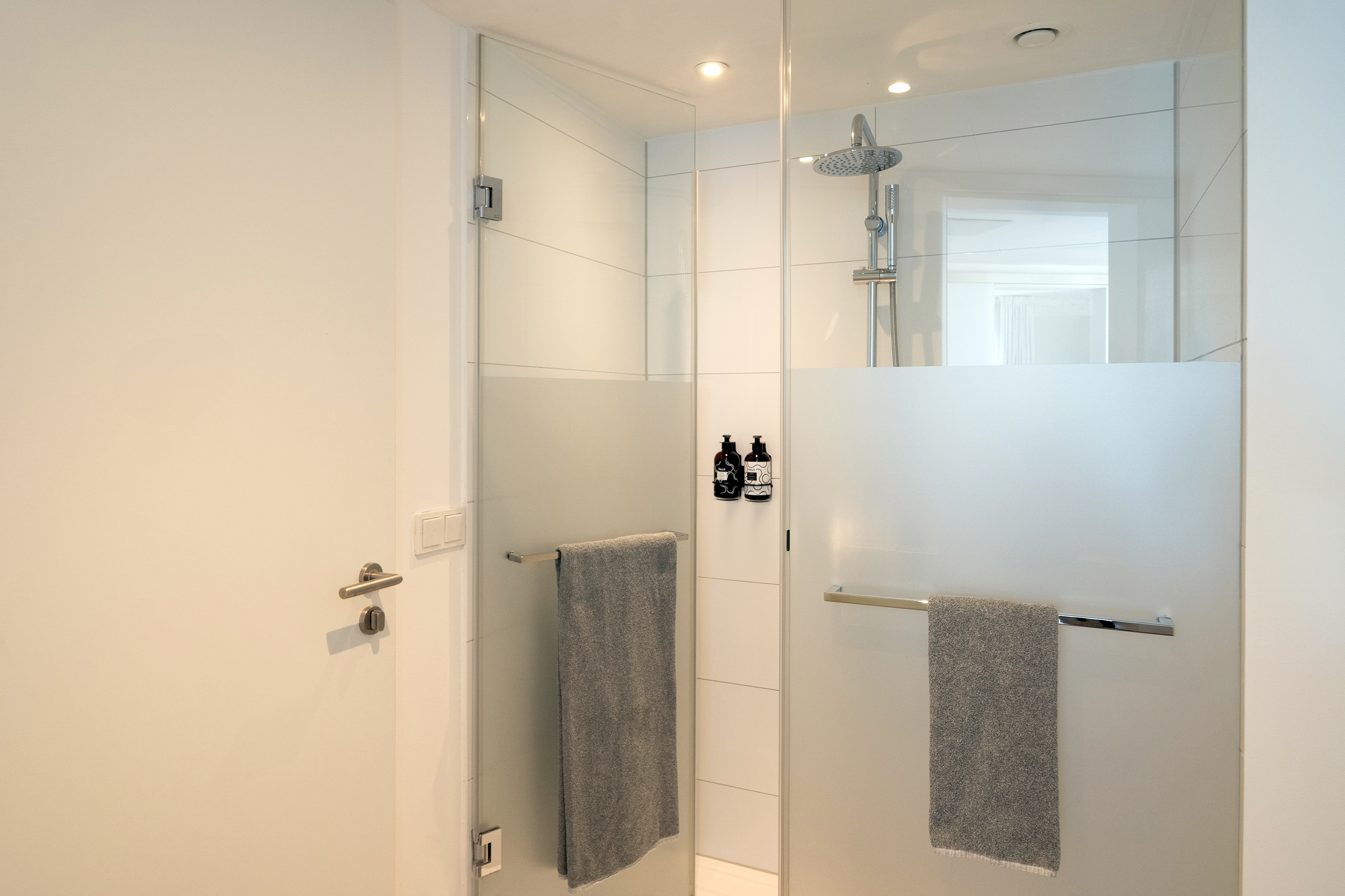 Modern glass shower cabin with frosted panels, rain shower, and grey towels.