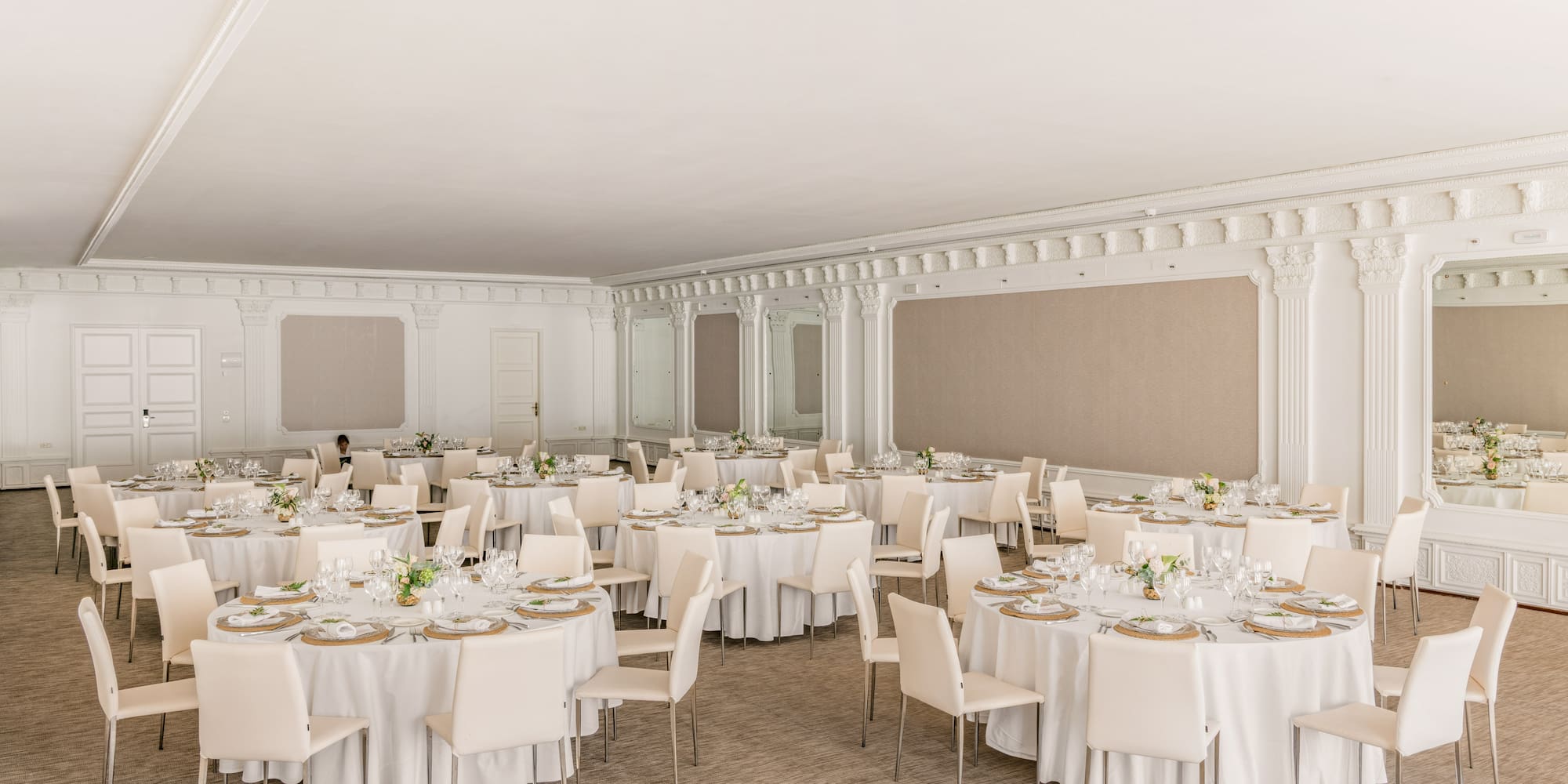 Elegant event hall with round tables, white chairs, and settings.