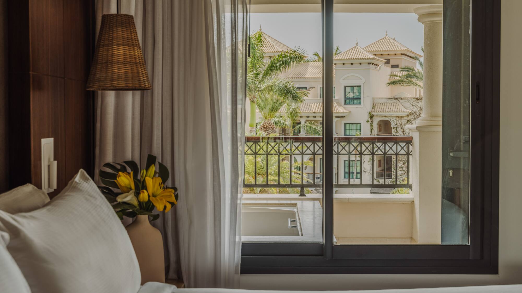 a bed with a vase of flowers and a lamp next to a window