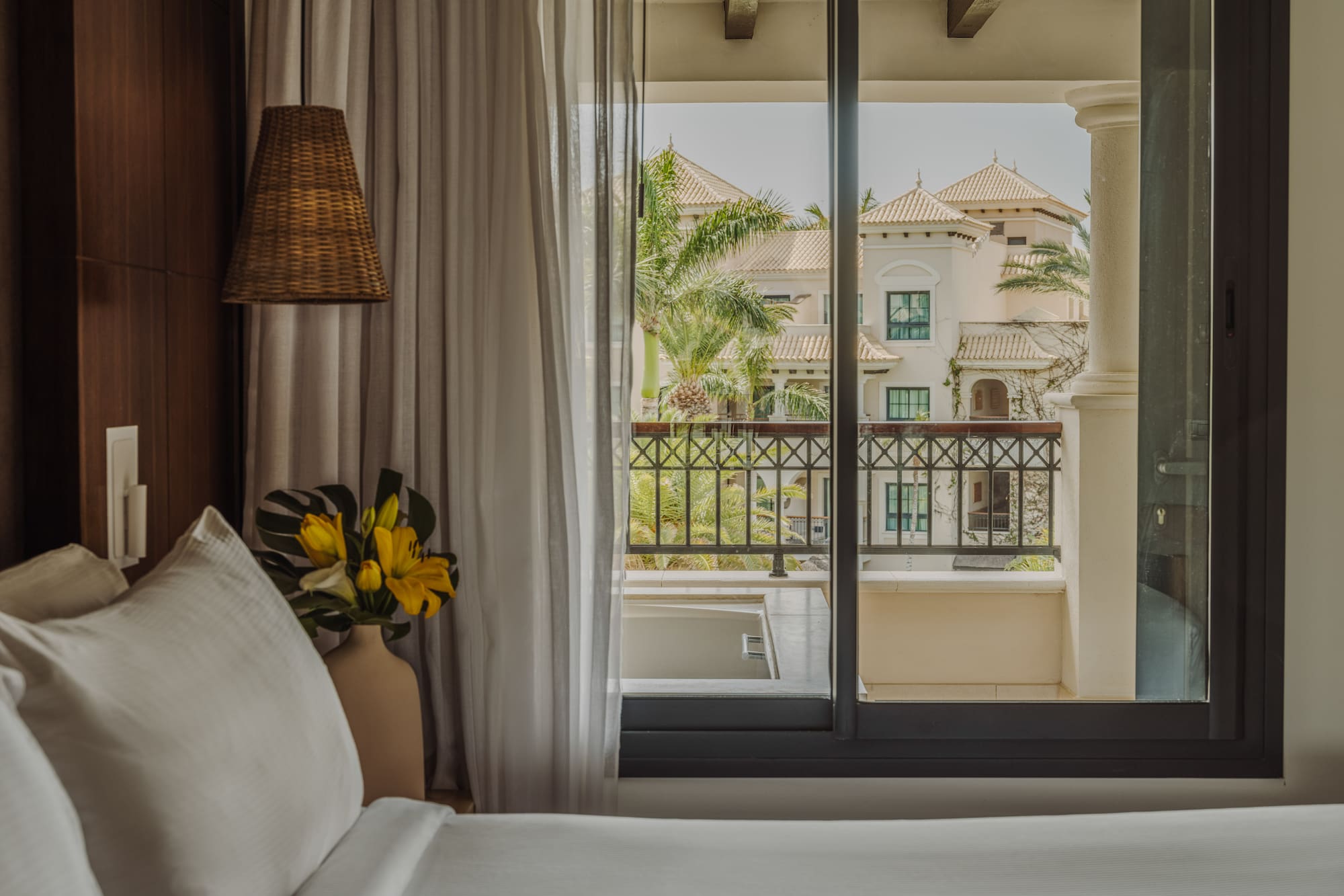 a bed with a vase of flowers and a lamp next to a window