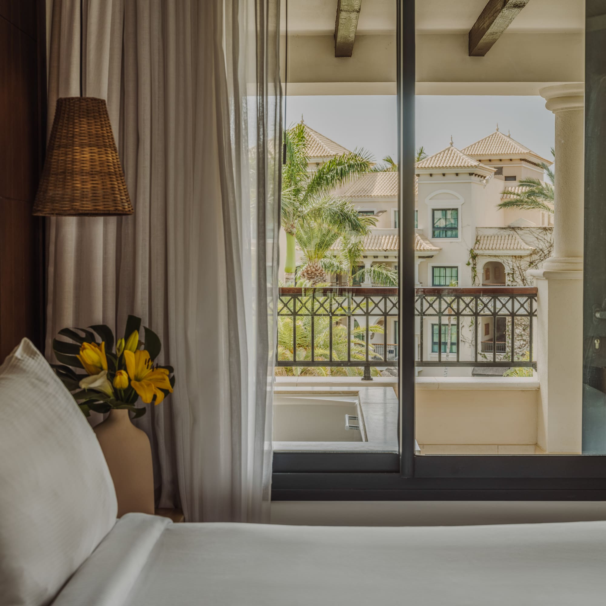 a bed with a vase of flowers and a lamp next to a window