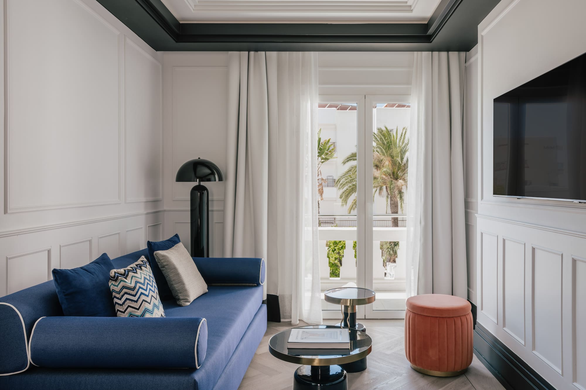 Elegant living room with blue sofa, modern decor, and balcony with palm trees.