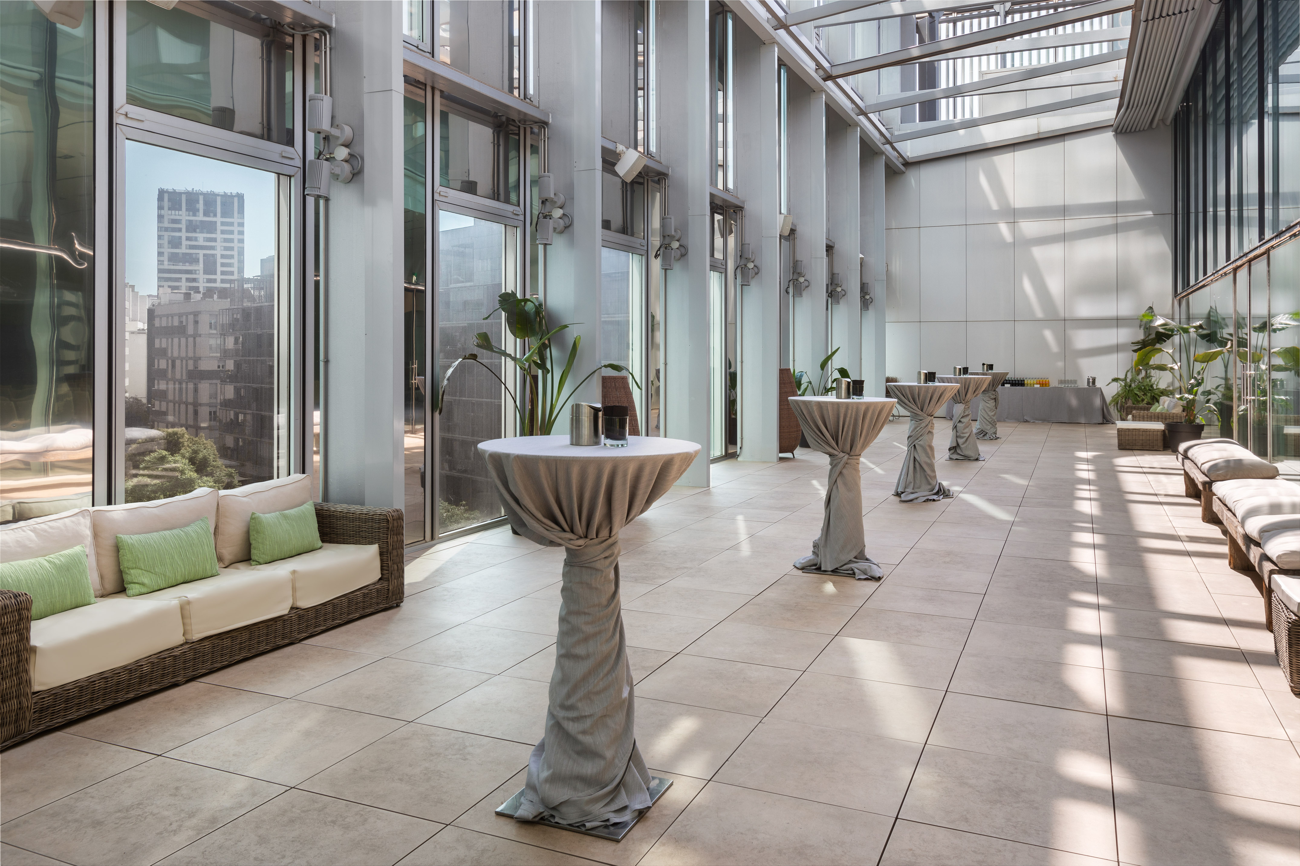 Spacious modern event venue with cocktail tables, sofas, plants, and city views. - Evolution-Terrace - Meliá Barcelona Sky, Barcelona