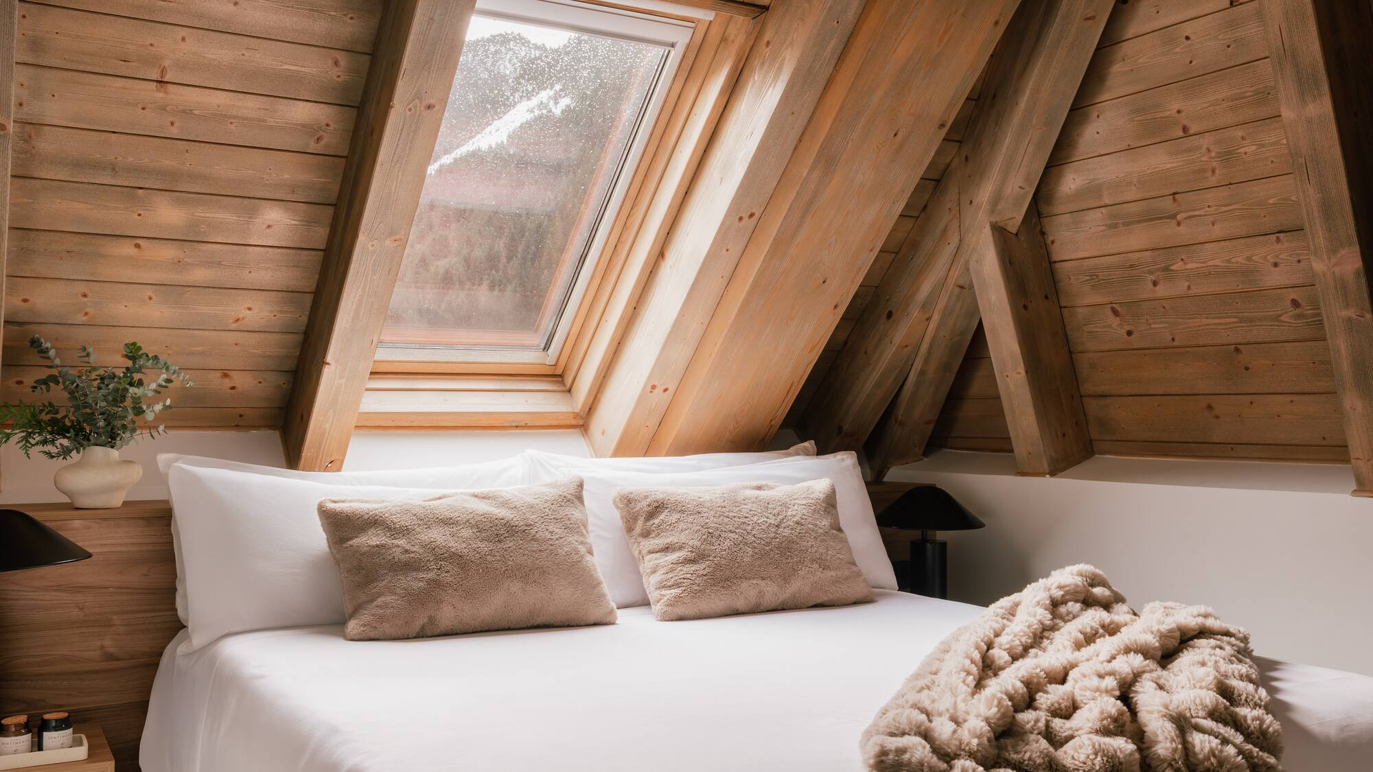 Rustic attic bedroom with wooden walls, skylight, and cozy white bed.