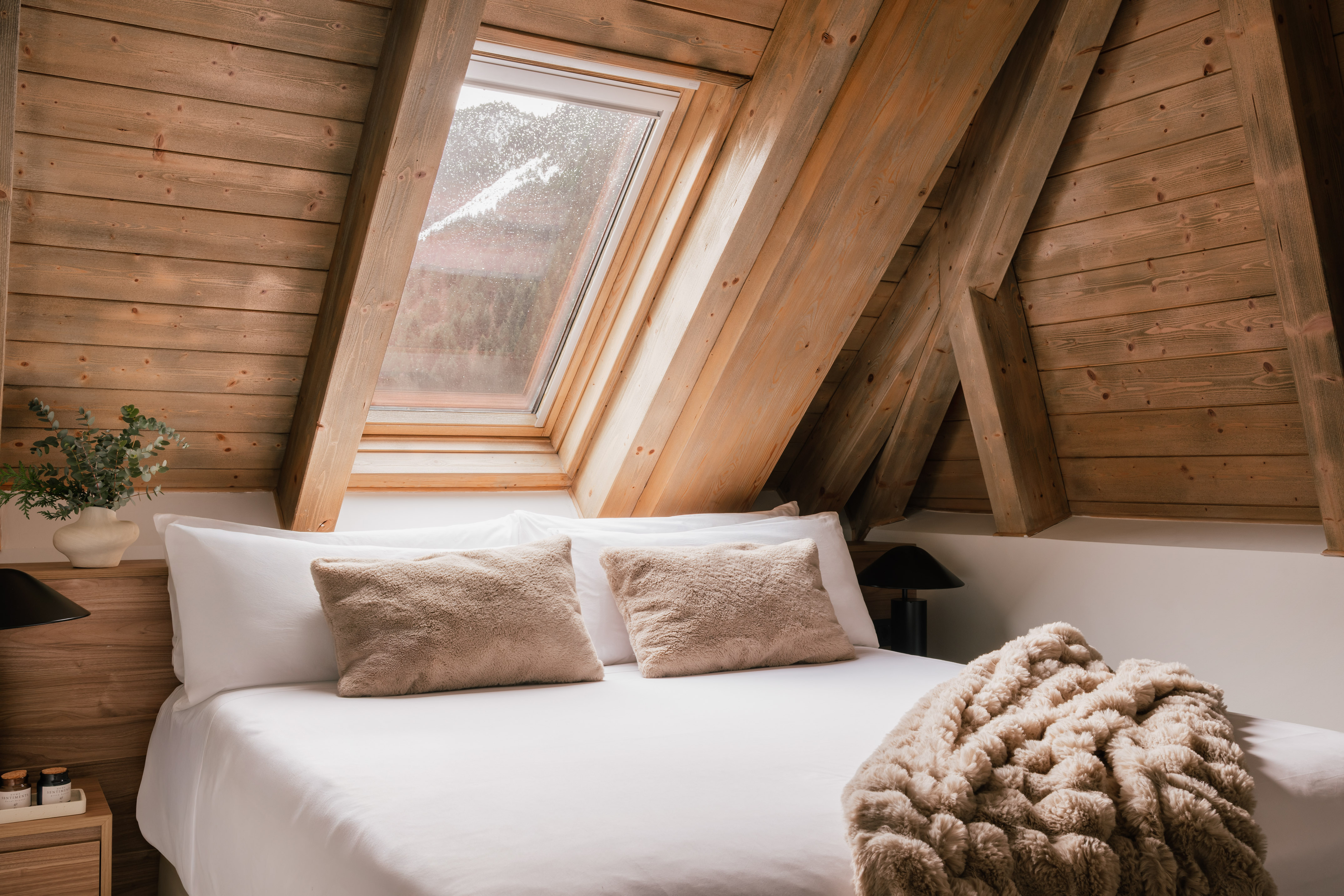 Rustic attic bedroom with wooden walls, skylight, and cozy white bed.