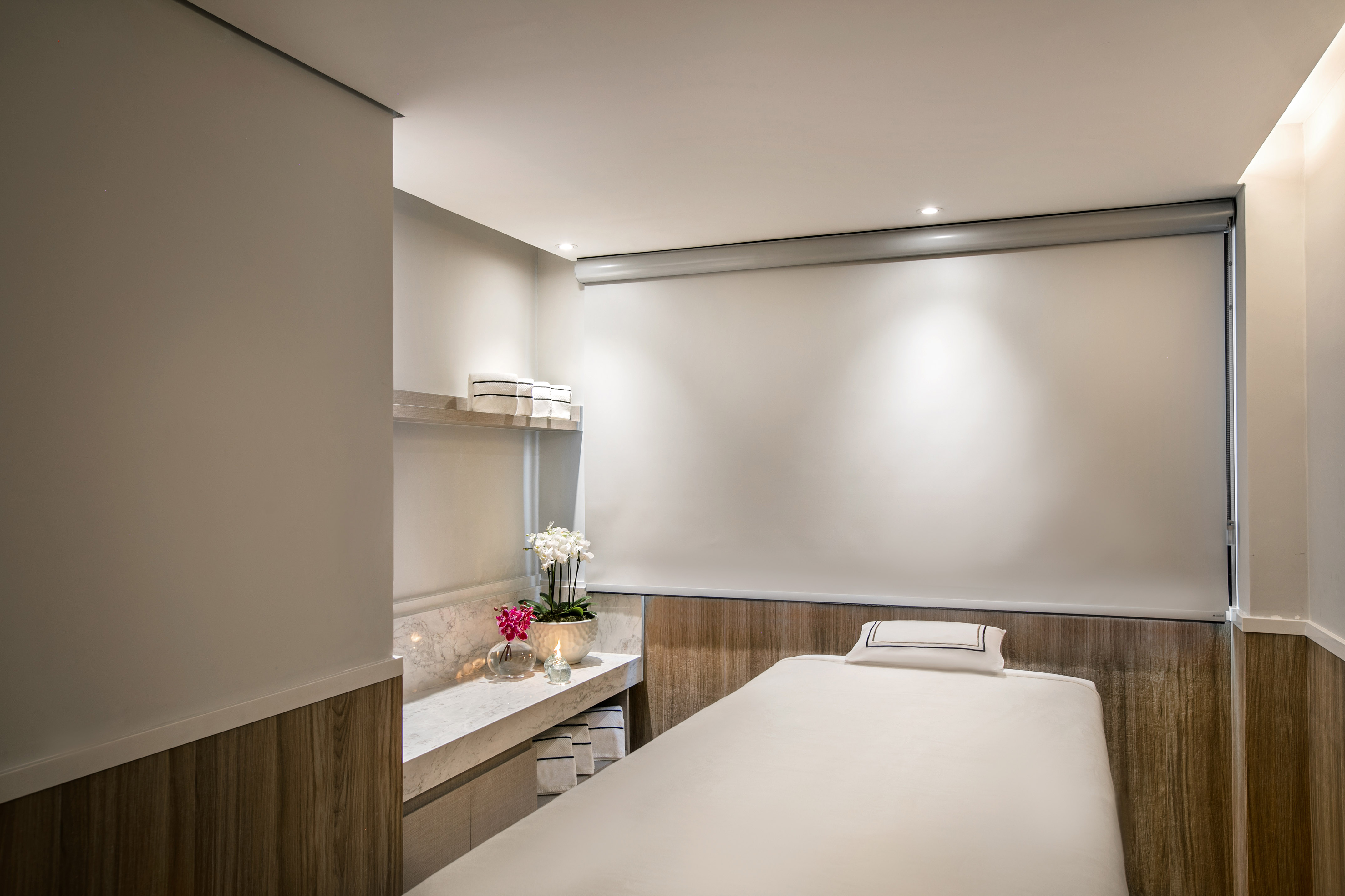 Bright spa massage room with white bed, marble counter, orchids, and towels.