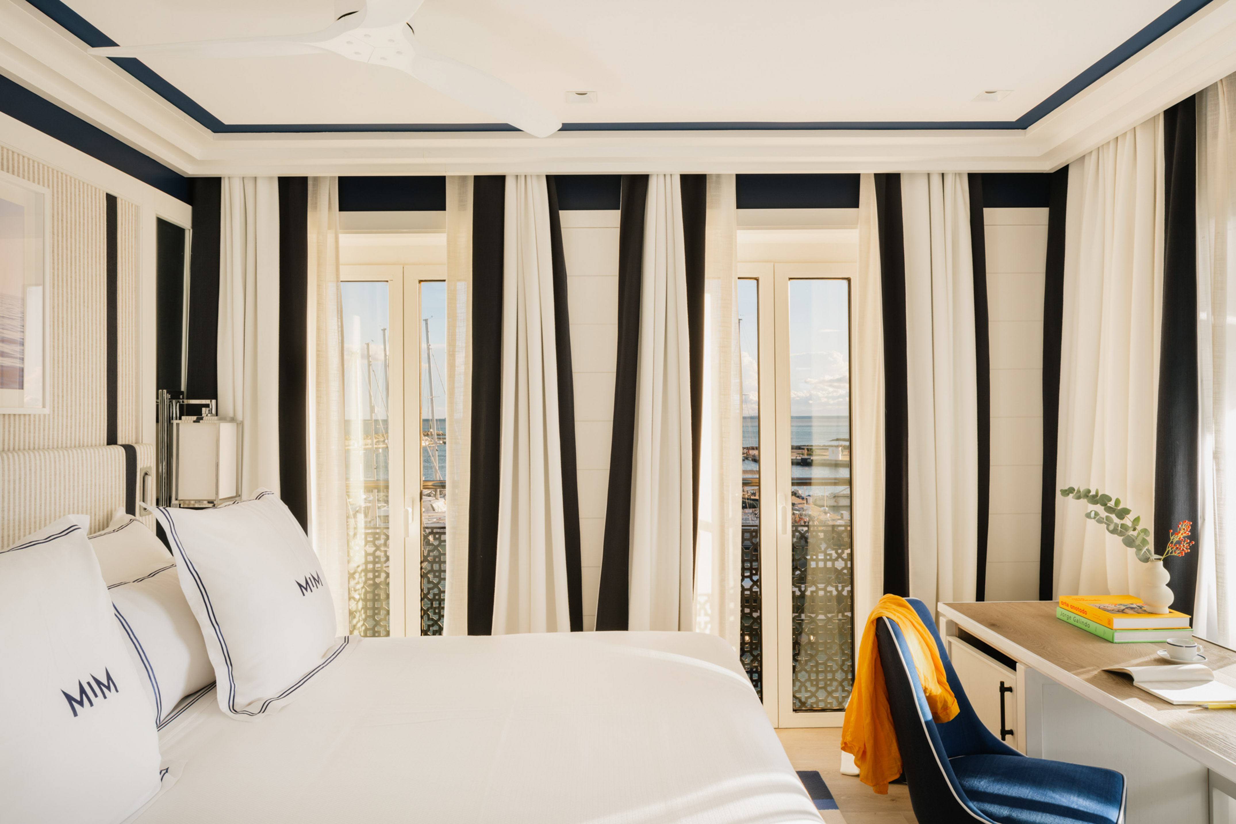 Hotel room with sea view, nautical navy and white decor, striped curtains.